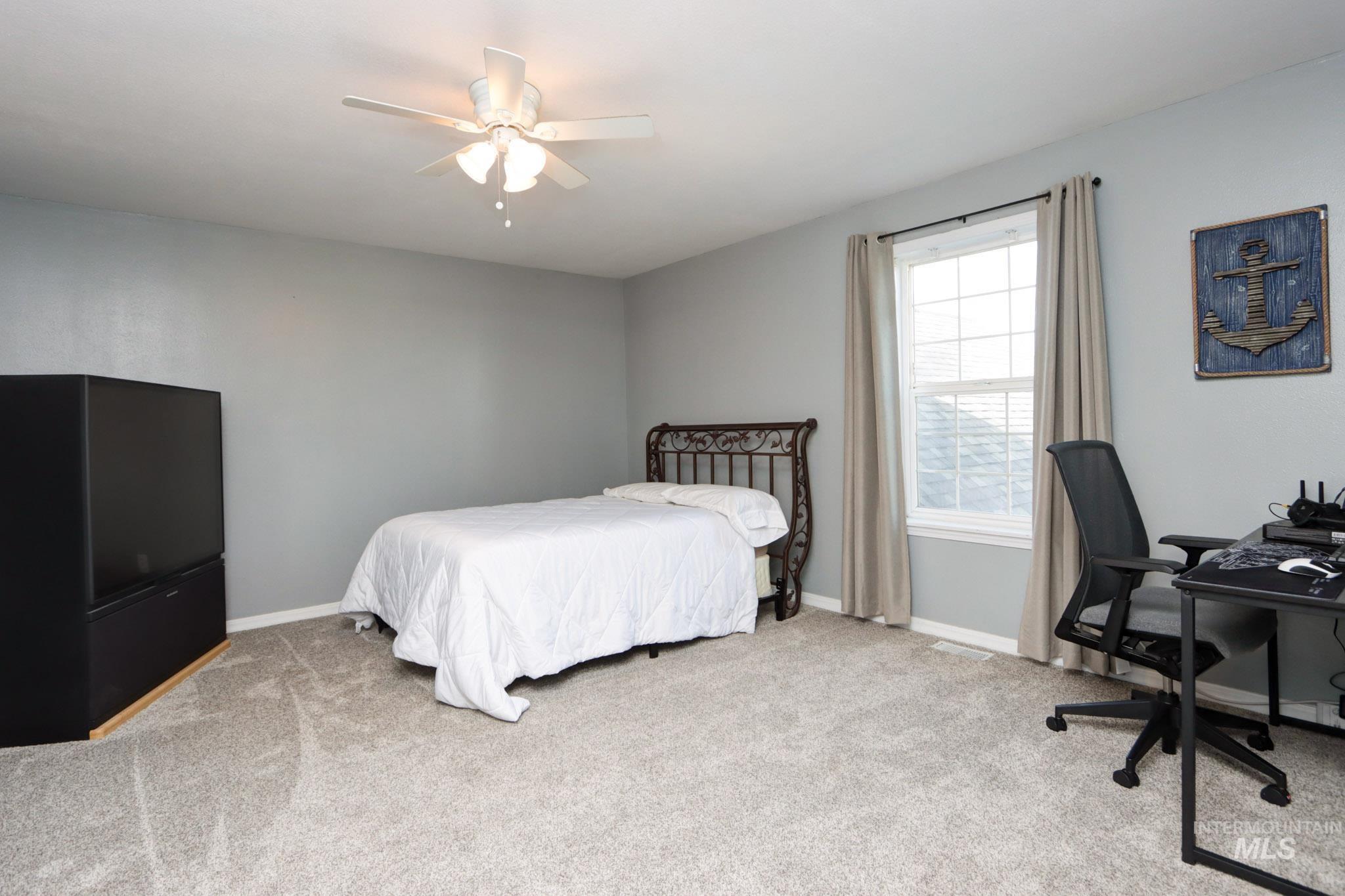 Bedroom with light carpet, a ceiling fan, and an office area