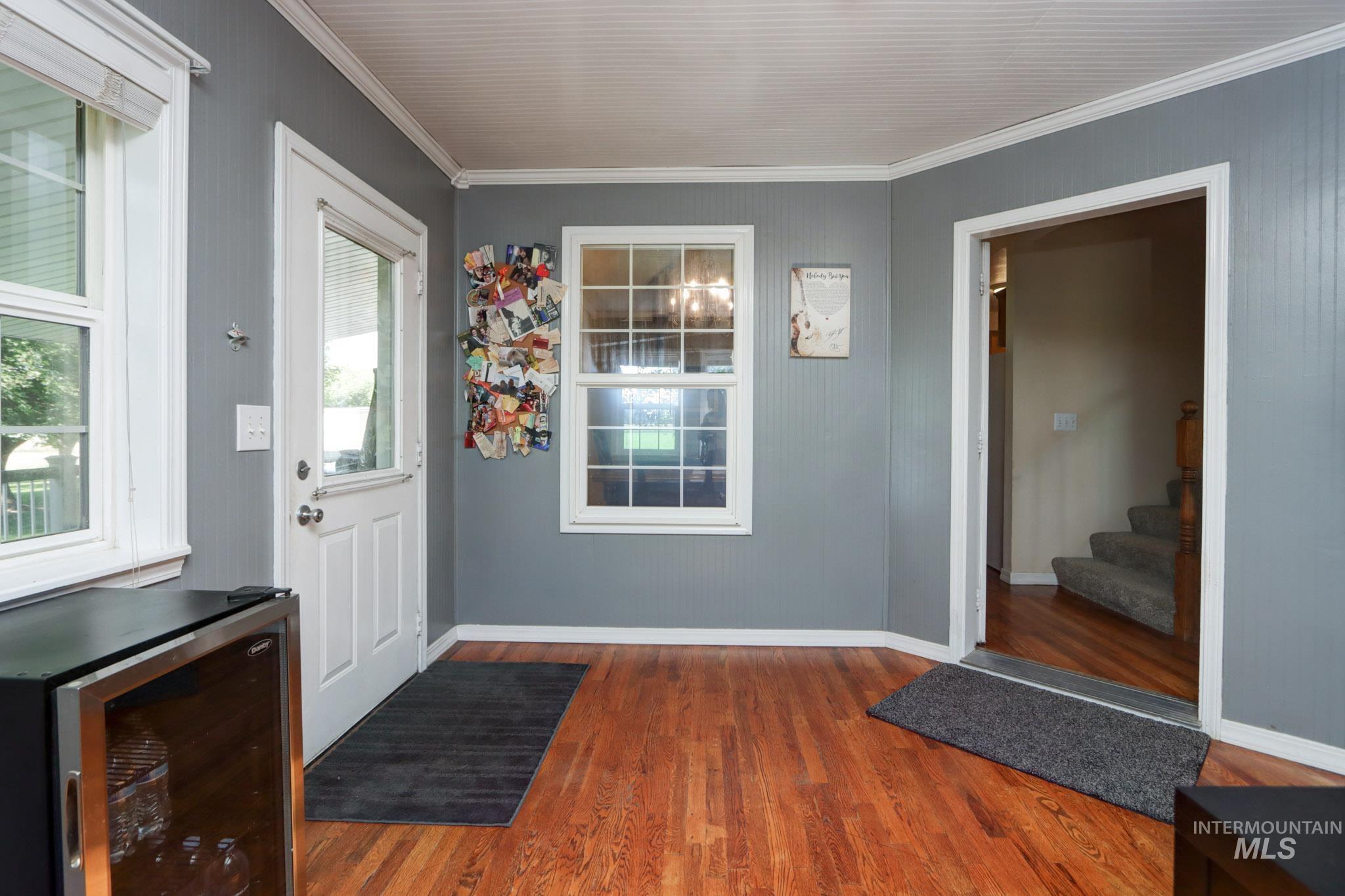 Foyer entrance with beverage cooler, wood finished floors, crown molding, and stairs
