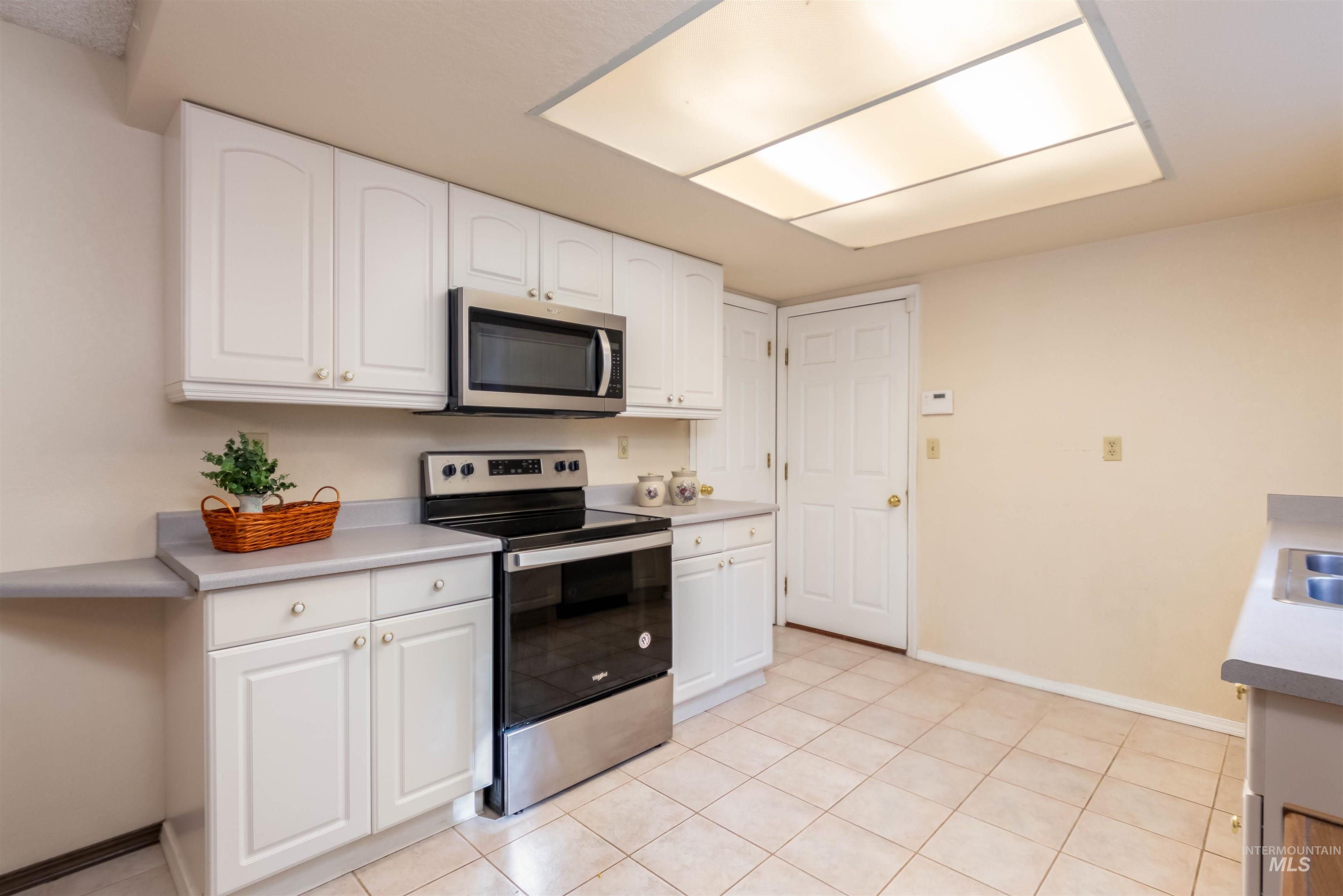 Kitchen featuring appliances with stainless steel finishes, light countertops, white cabinetry, and light tile patterned floors
