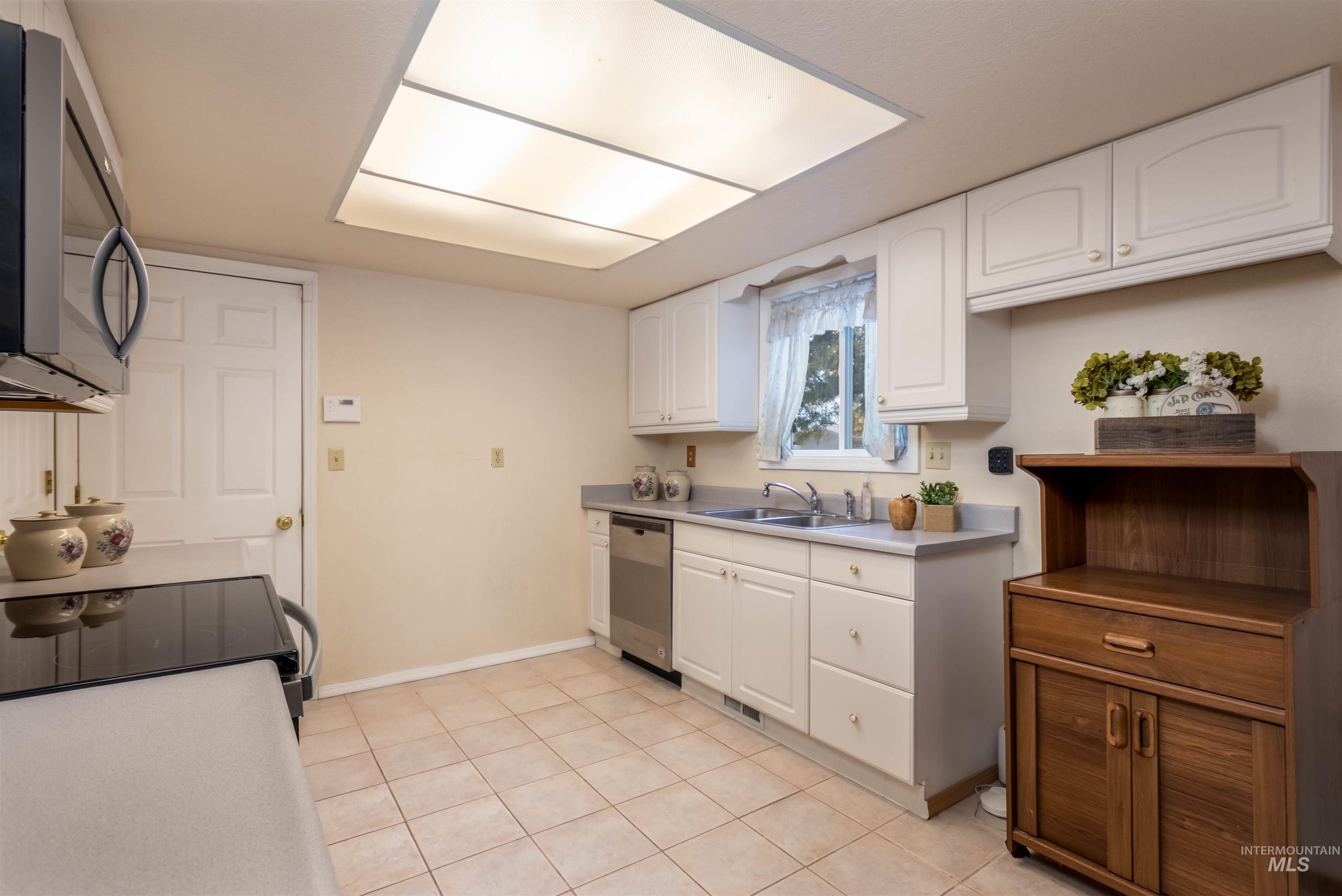 Kitchen featuring white cabinetry, appliances with stainless steel finishes, light tile patterned floors, and light countertops