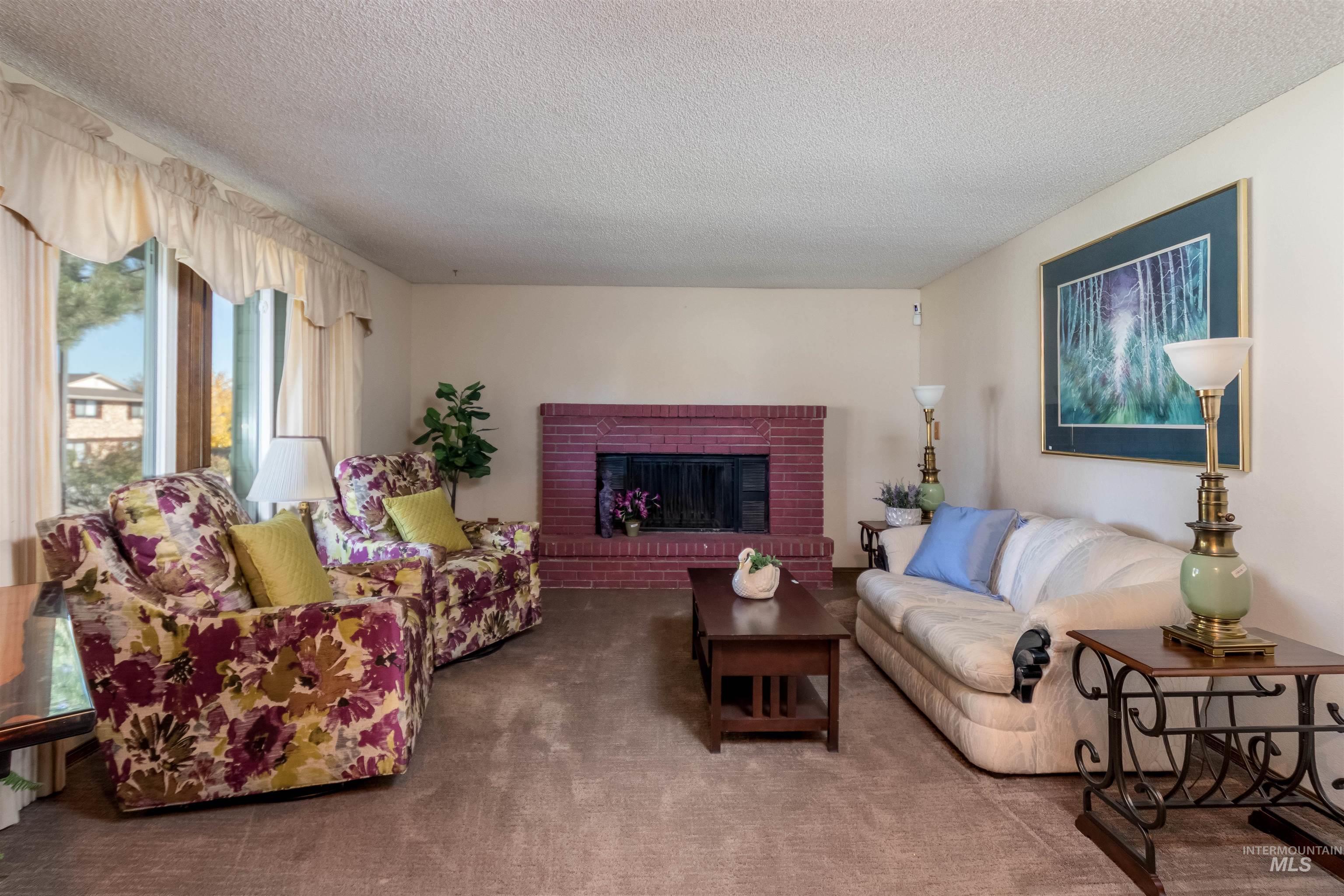 Carpeted living room featuring a brick fireplace and a textured ceiling