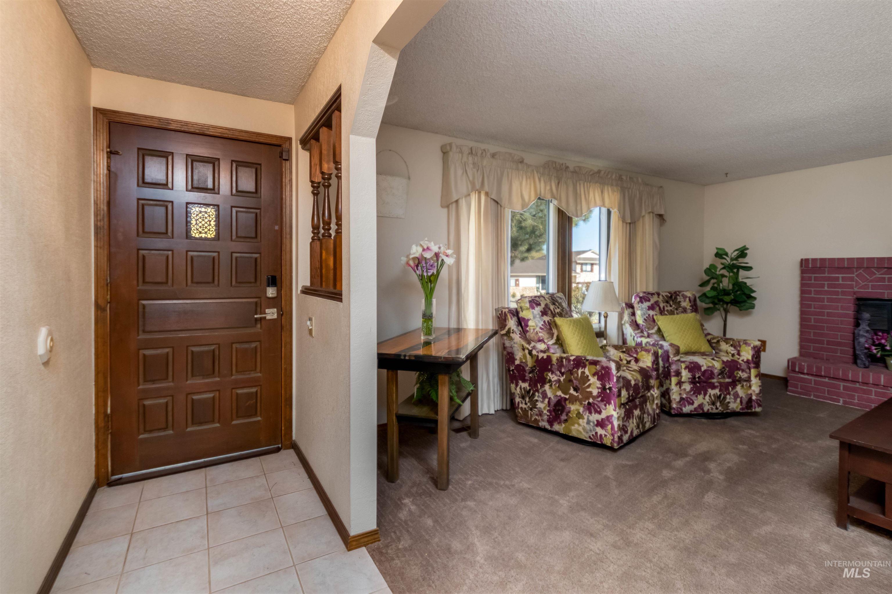 Foyer entrance with a textured ceiling, a brick fireplace, light tile patterned floors, and light colored carpet