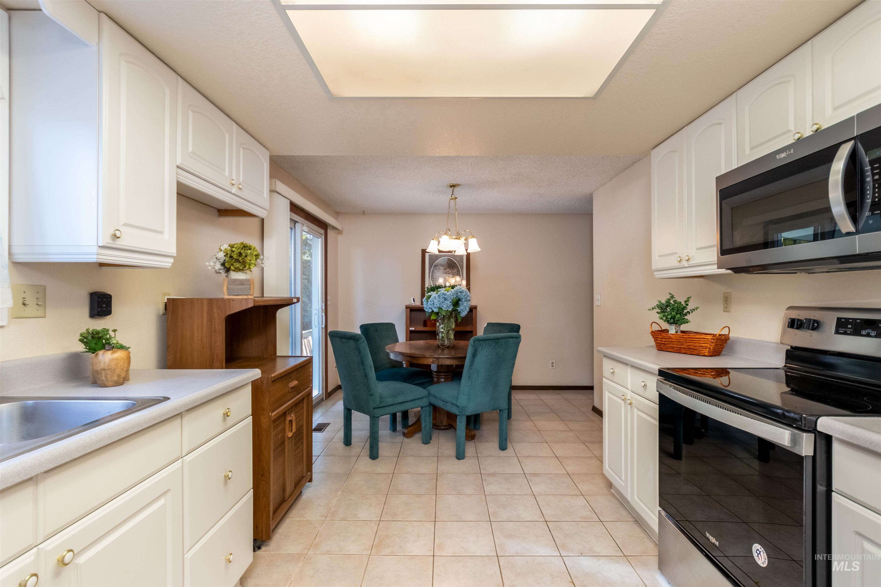 Kitchen with appliances with stainless steel finishes, pendant lighting, white cabinetry, a chandelier, and light countertops