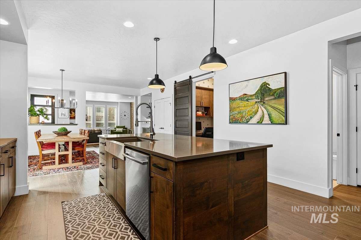 Kitchen with a barn door, dark wood finish cabinets, dark wood finished floors, decorative light fixtures, and dishwasher