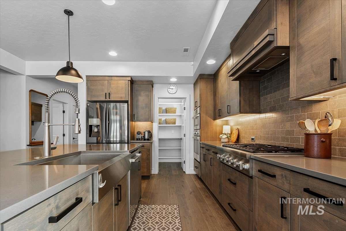 Kitchen featuring stainless steel appliances, decorative backsplash, dark wood-style flooring, pendant lighting, and dark wood finish cabinetry