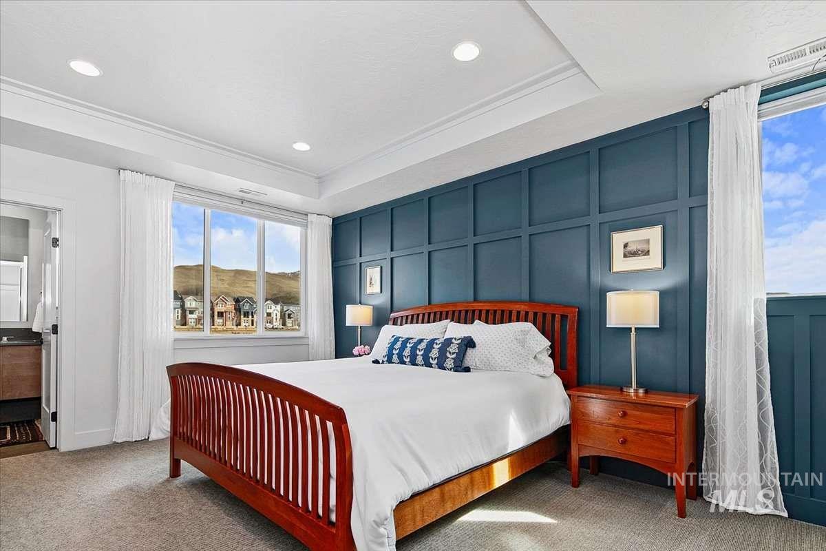 Bedroom with a decorative wall, light carpet, a tray ceiling, and recessed lighting