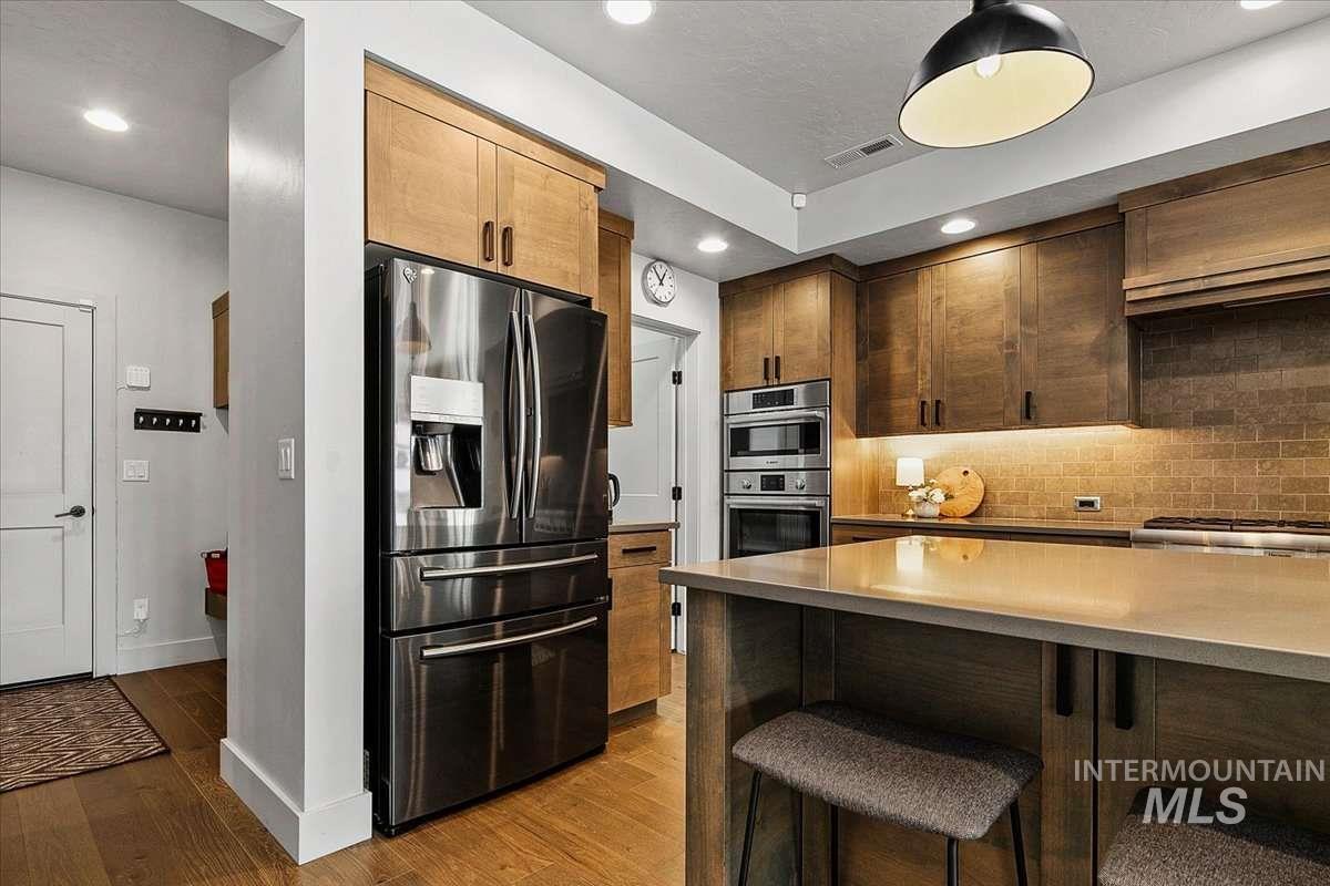Kitchen with stainless steel appliances, decorative backsplash, dark wood-style floors, a breakfast bar area, and recessed lighting