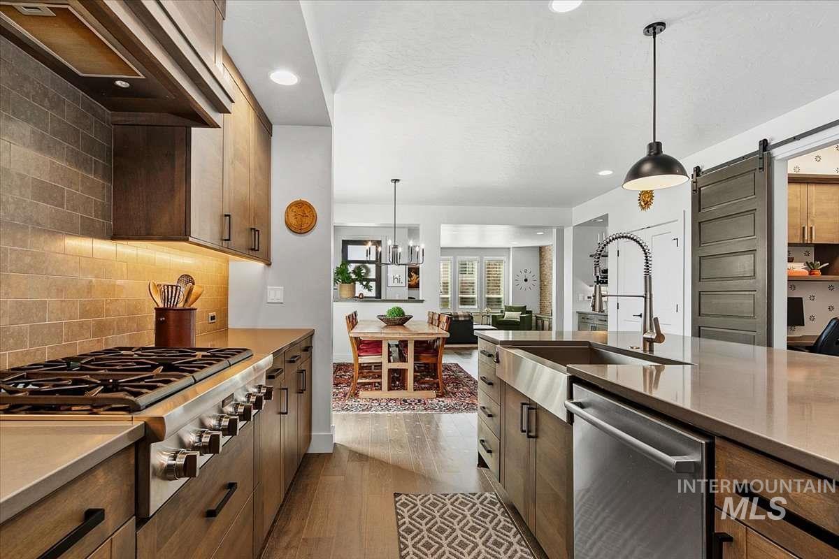 Kitchen with stainless steel appliances, a barn door, pendant lighting, dark wood-style flooring, and light stone countertops