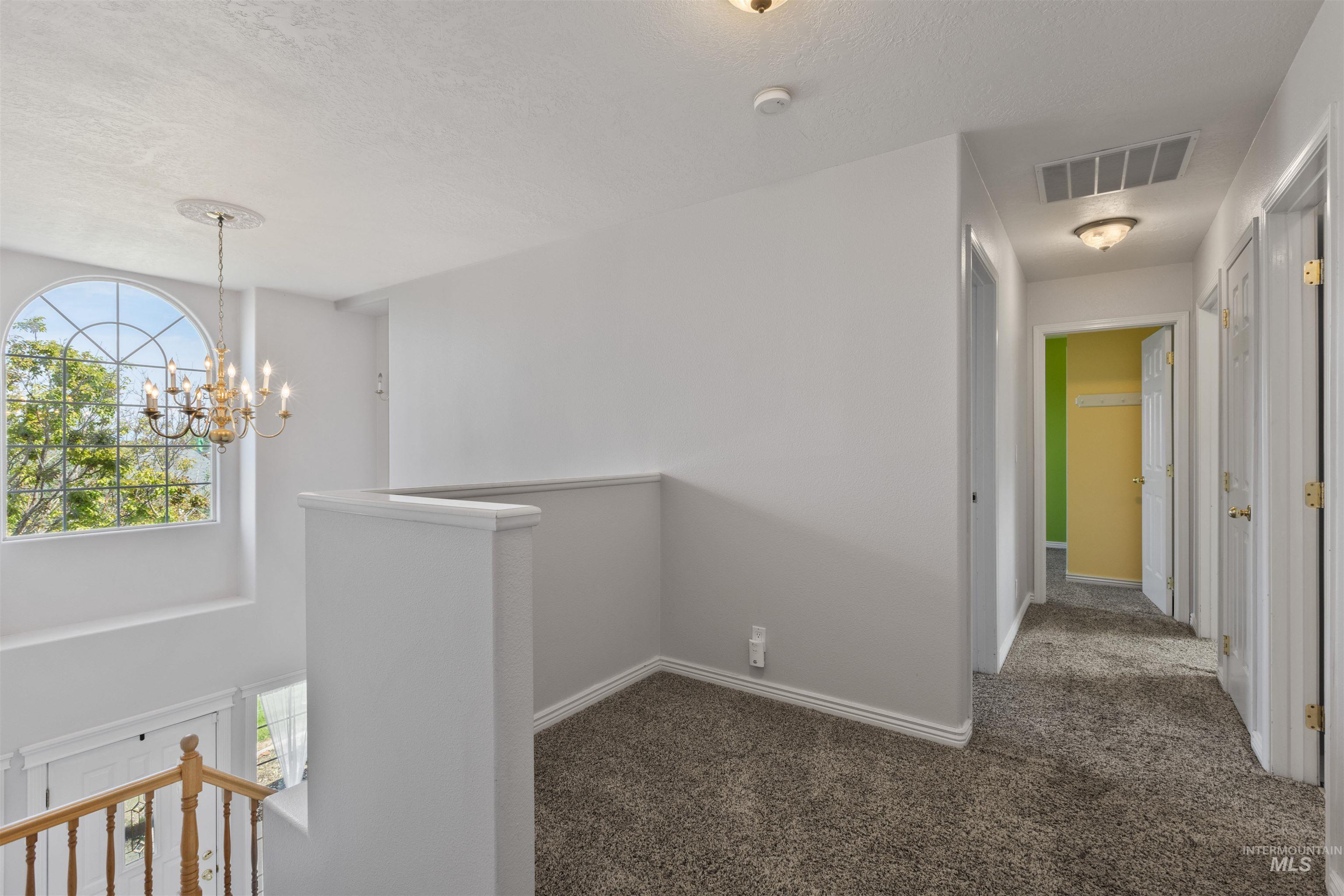 Hallway featuring an upstairs landing, carpet floors, a chandelier, and a textured ceiling