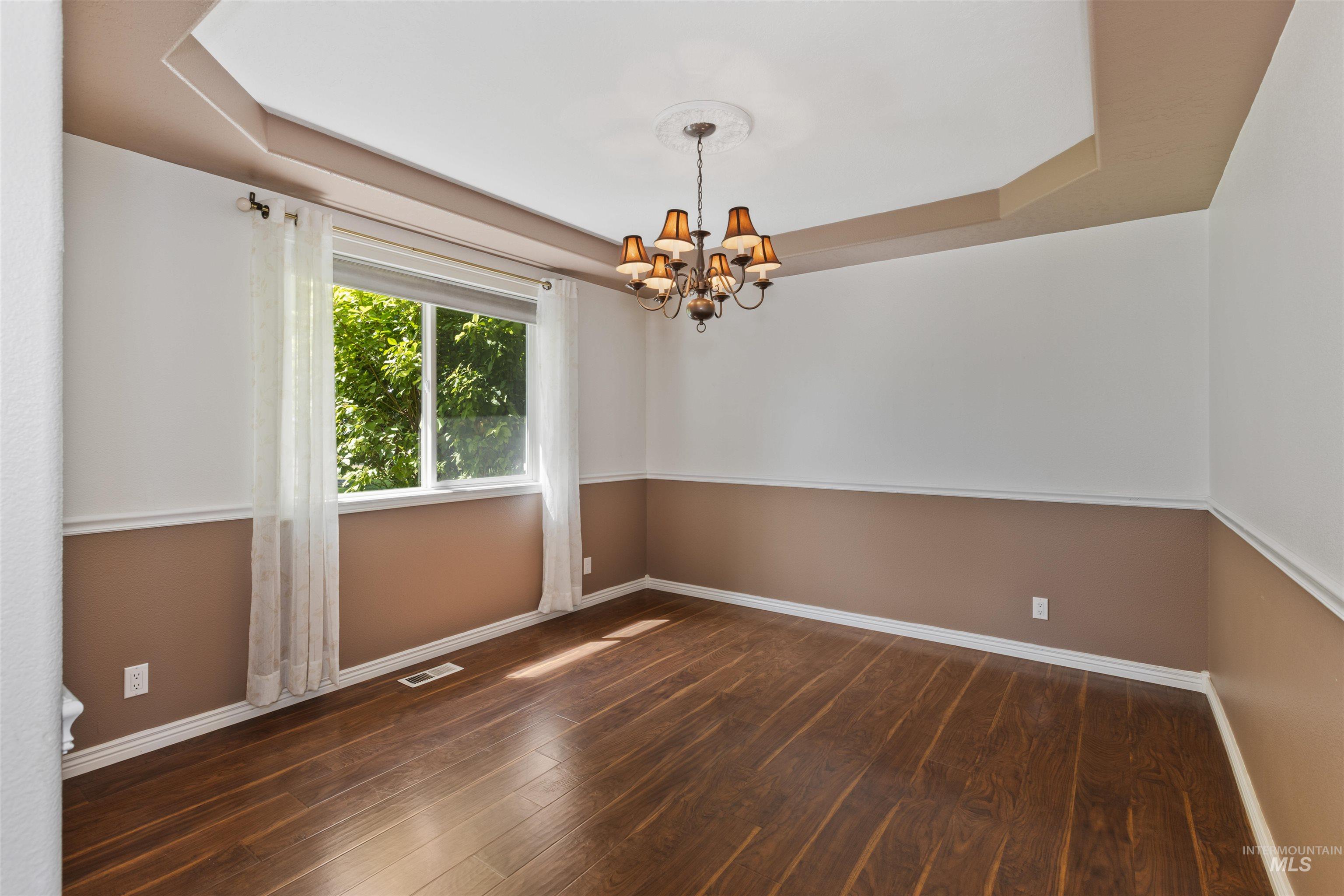 Spare room with a raised ceiling, dark wood finished floors, and a chandelier