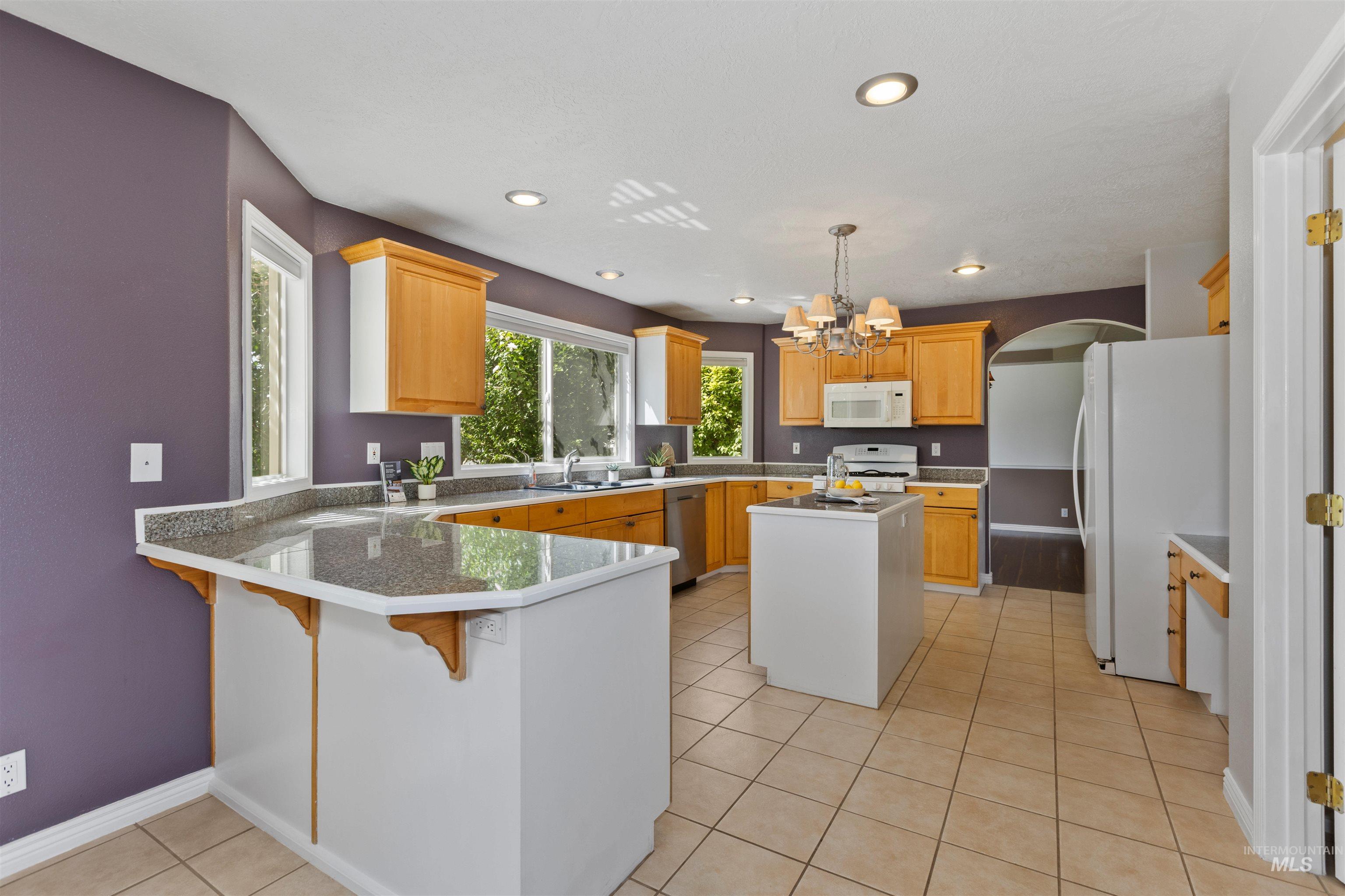 Kitchen featuring light tile patterned floors, white appliances, a kitchen breakfast bar, a peninsula, and a chandelier