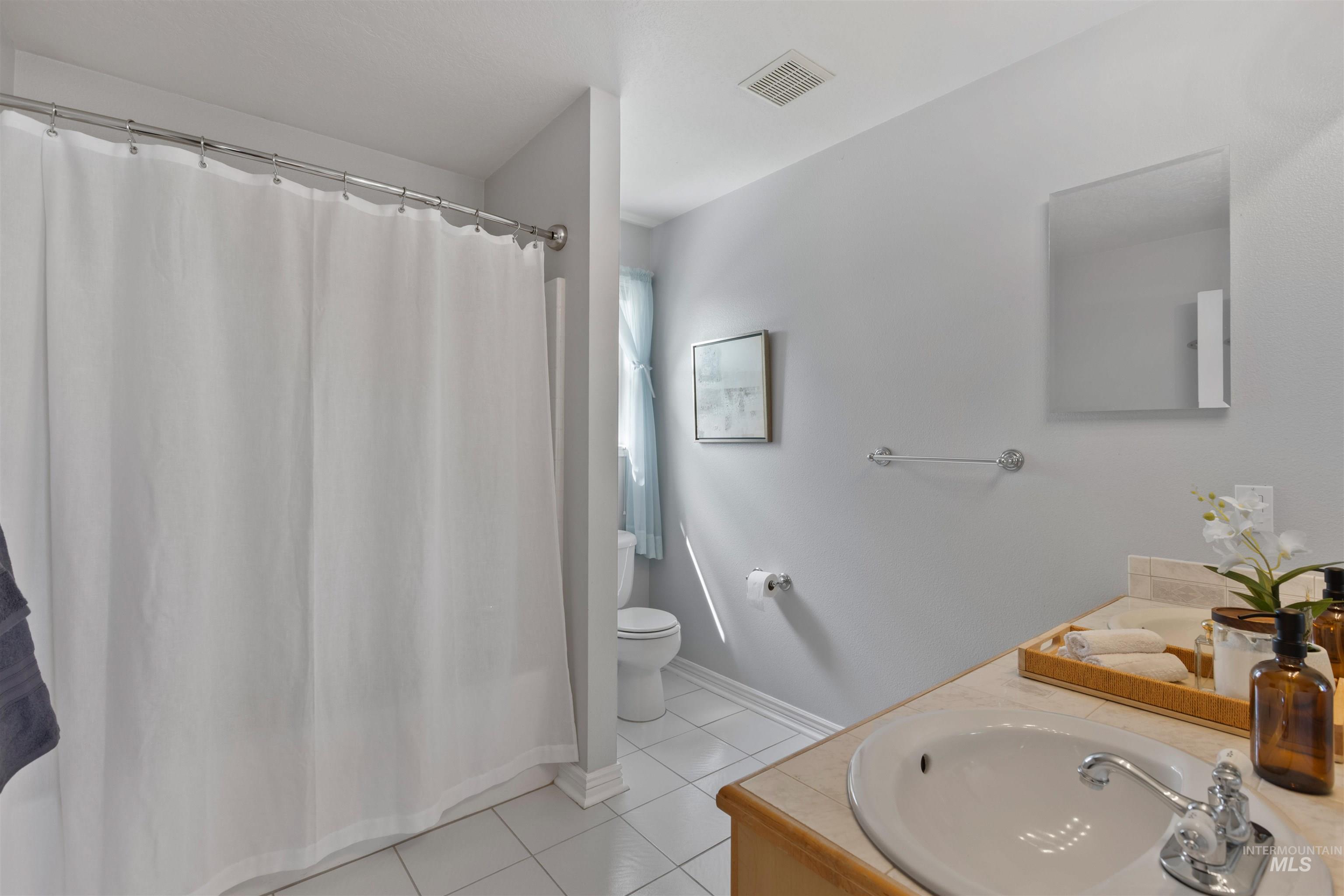 Full bathroom featuring light tile patterned floors, vanity, and curtained shower