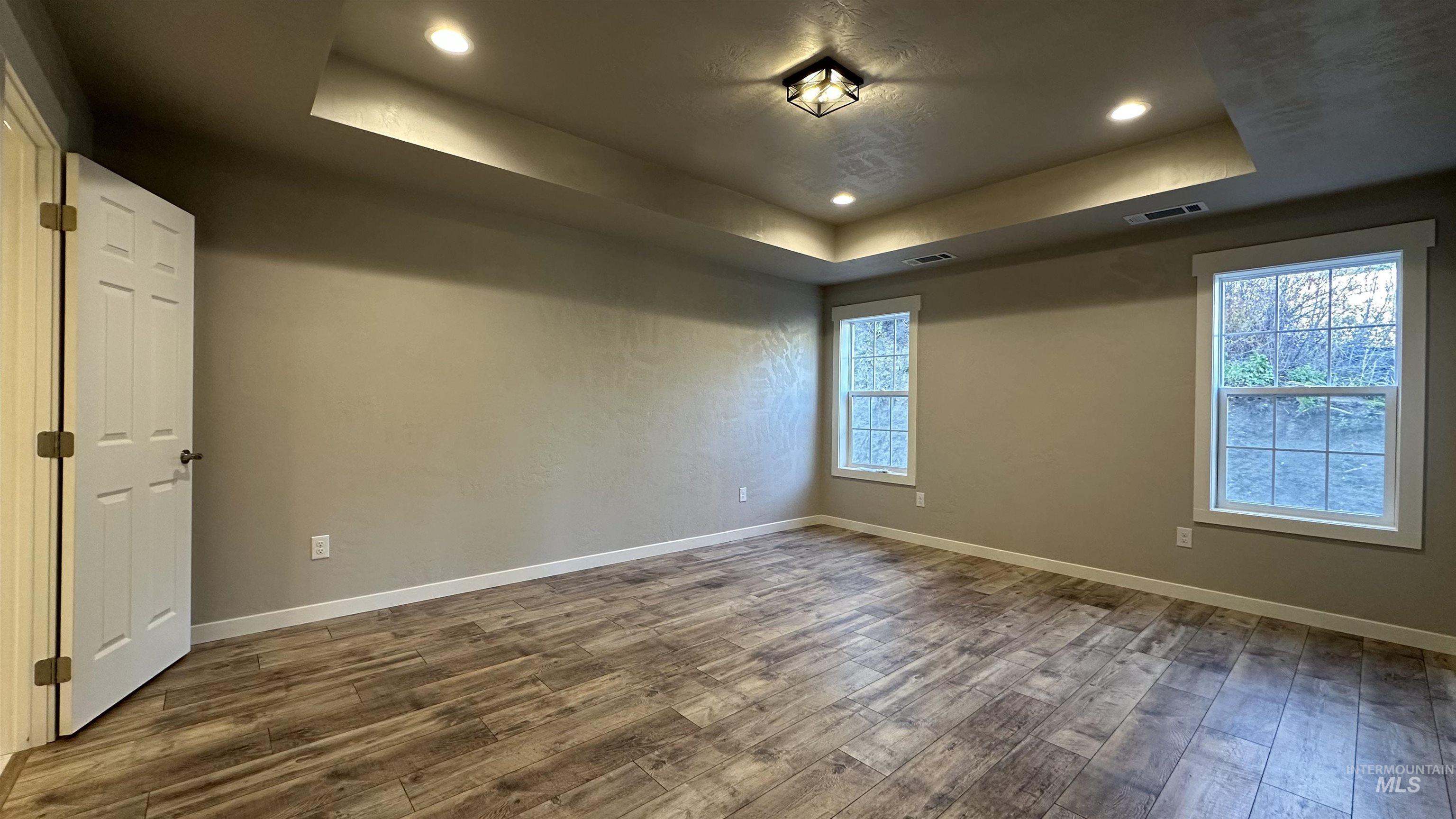 Spare room featuring a raised ceiling, plenty of natural light, wood finished floors, and recessed lighting