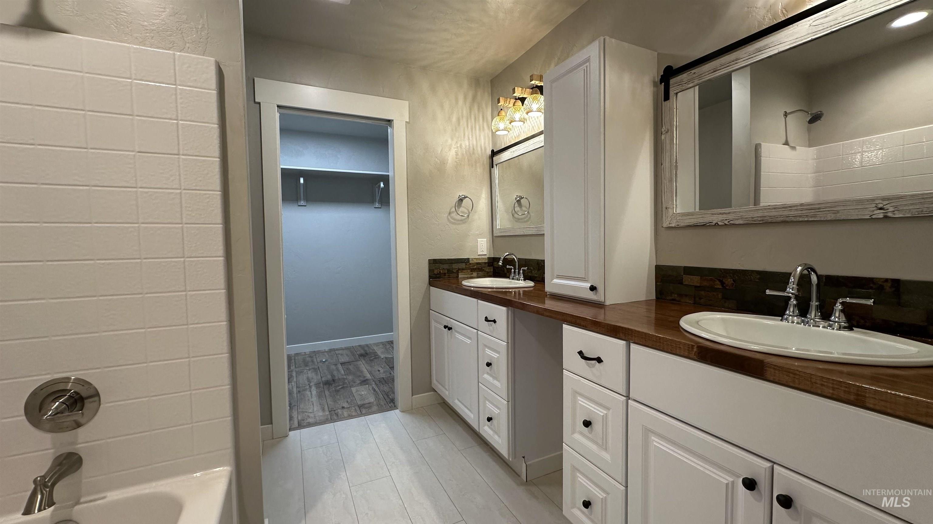 Full bath featuring double vanity, light wood-style flooring, a textured wall, and bathtub / shower combination