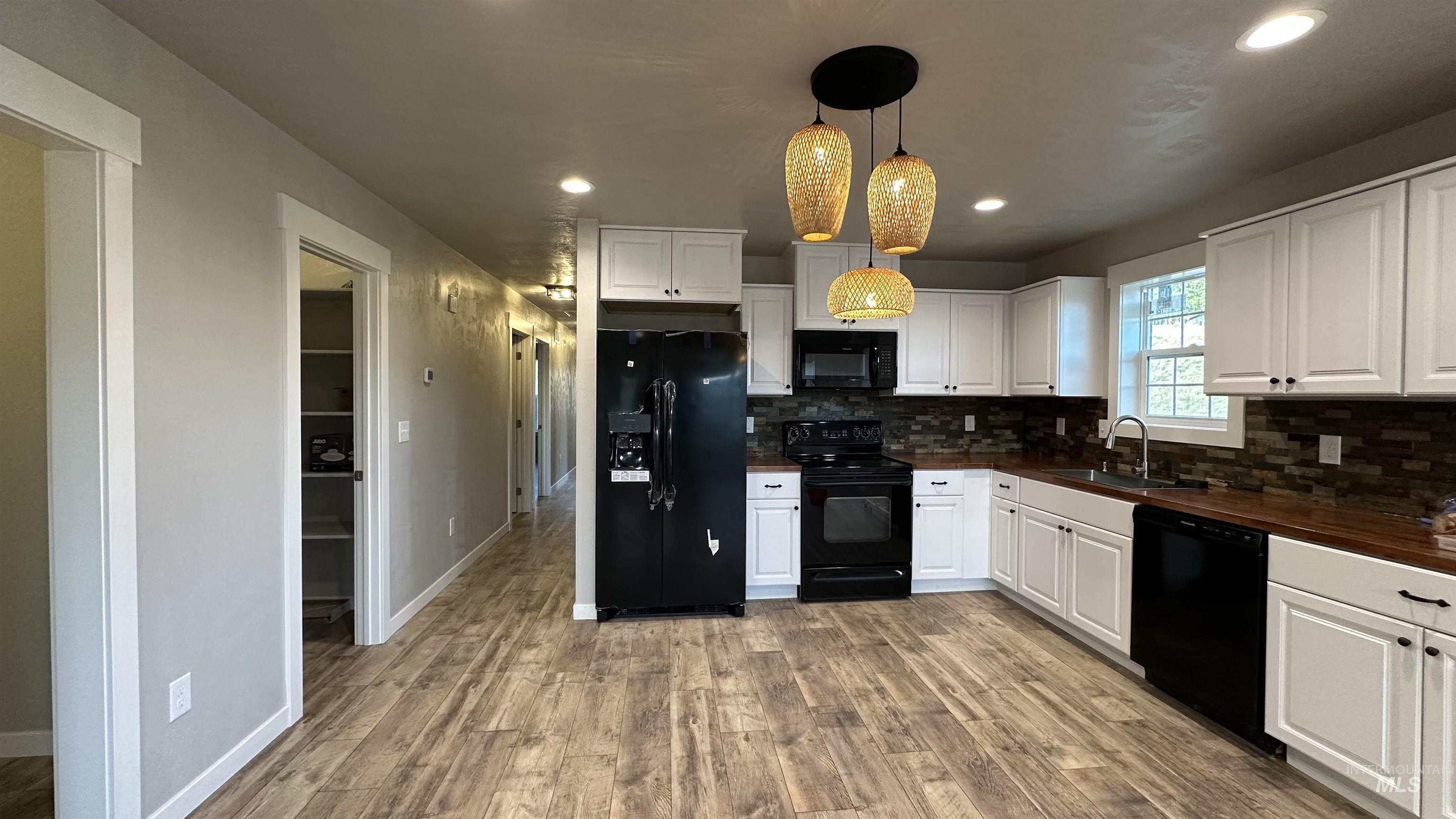 Kitchen with black appliances, white cabinetry, butcher block countertops, tasteful backsplash, and recessed lighting