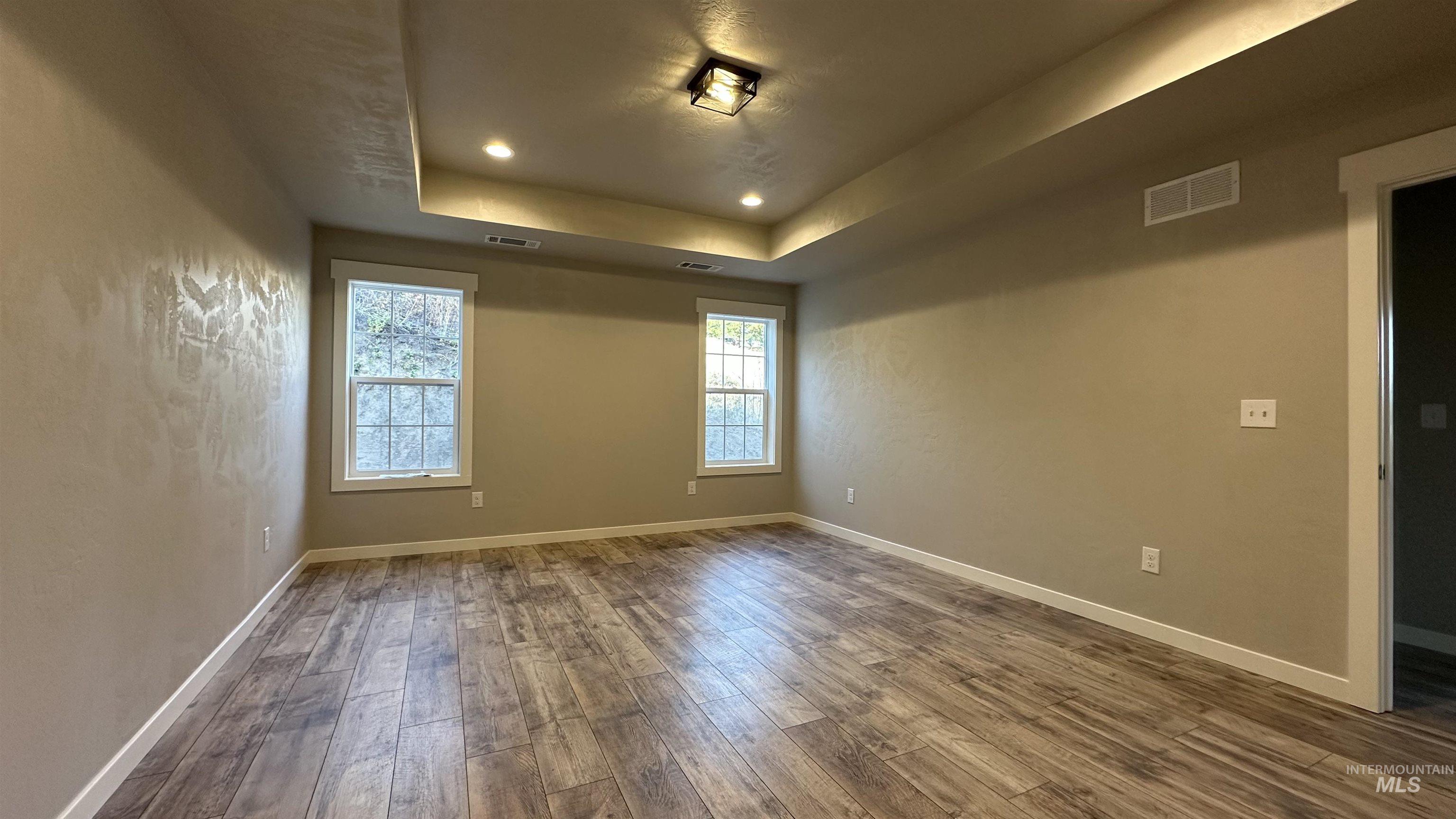Empty room with a tray ceiling, dark wood-style floors, and recessed lighting
