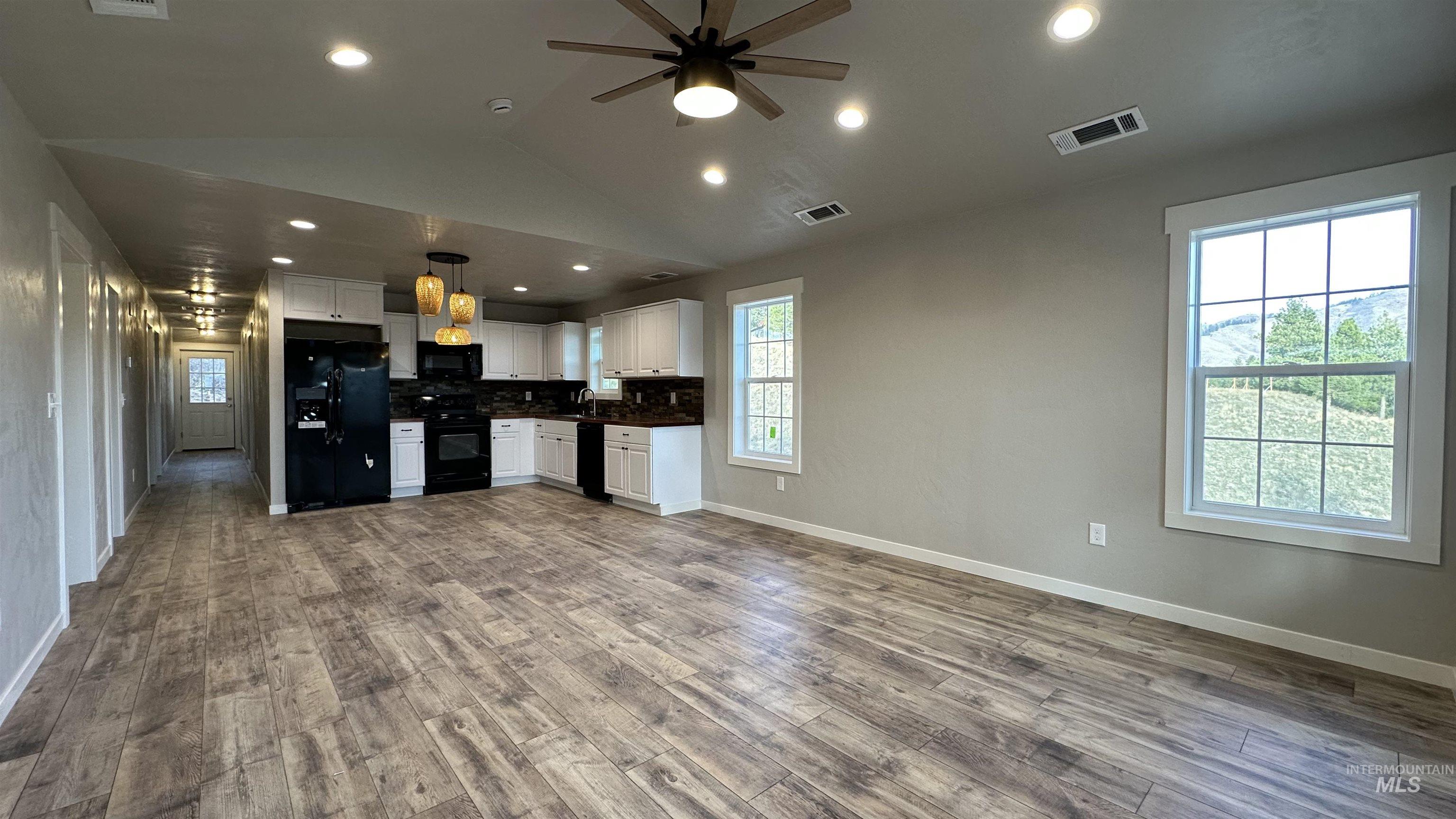 Kitchen with backsplash, white cabinets, vaulted ceiling, black appliances, and a ceiling fan