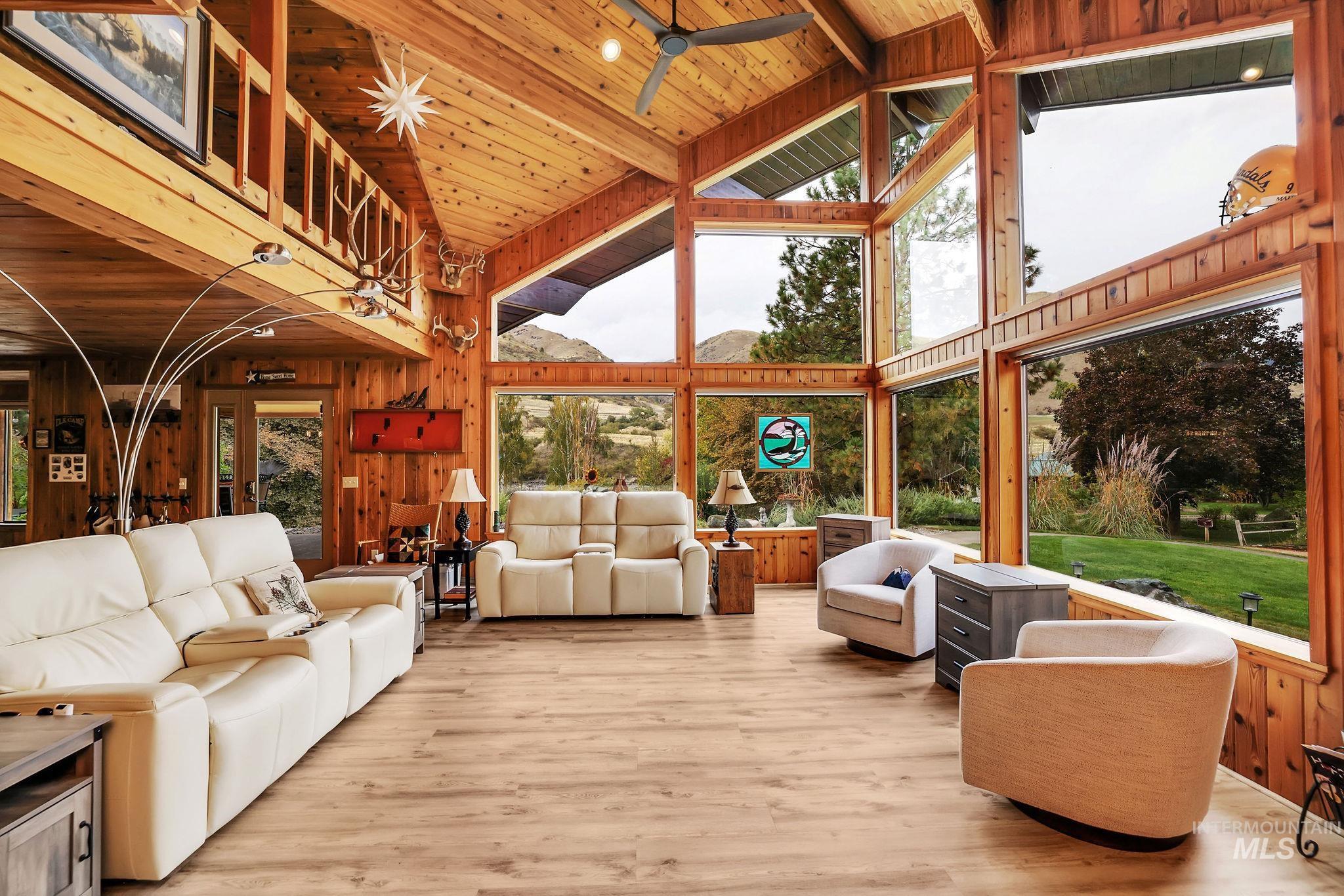 Living room with high vaulted ceiling, wood walls, a wood ceiling with exposed beams, light wood-style flooring, and a ceiling fan