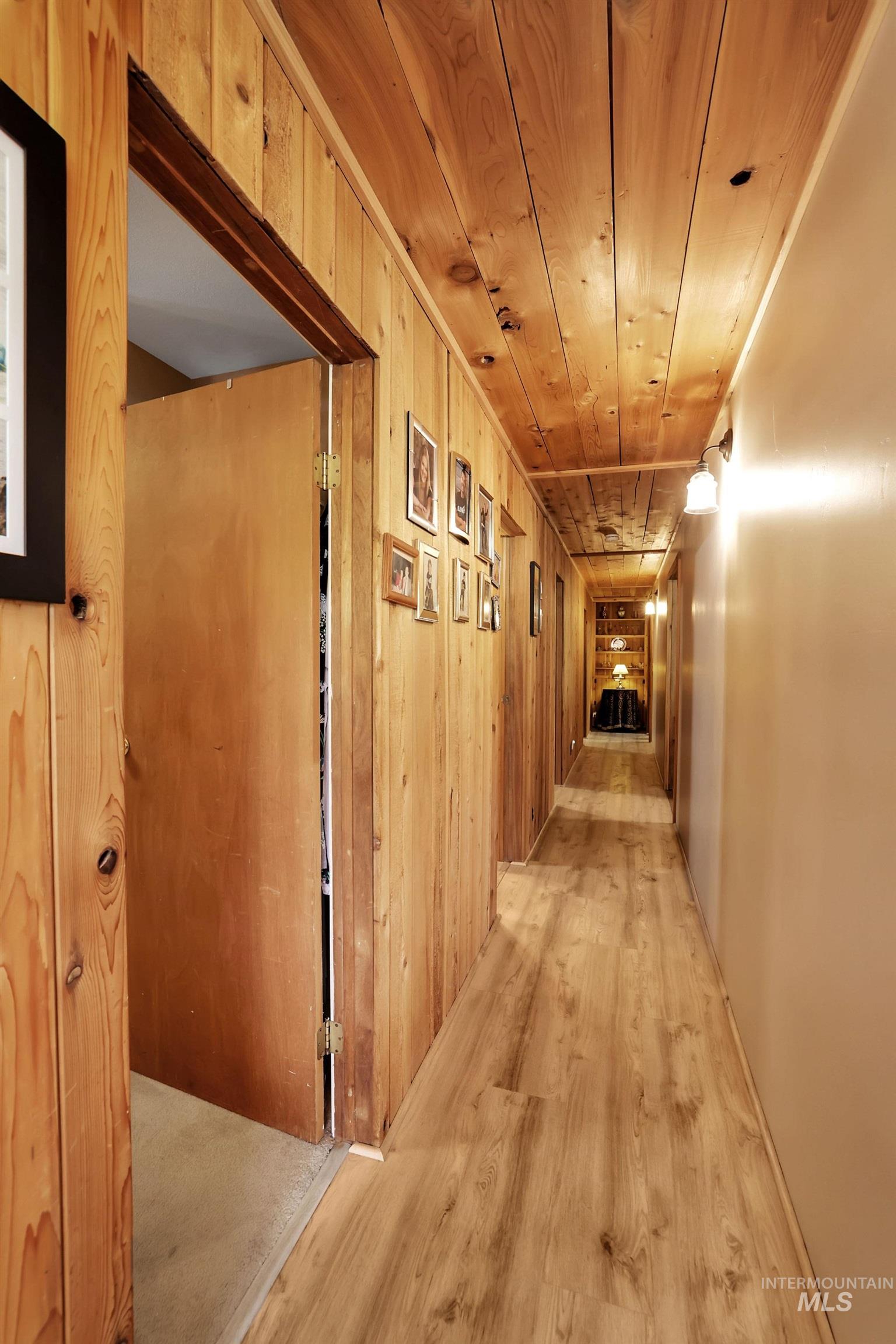 Hallway featuring light wood-type flooring, wooden walls, and wood ceiling
