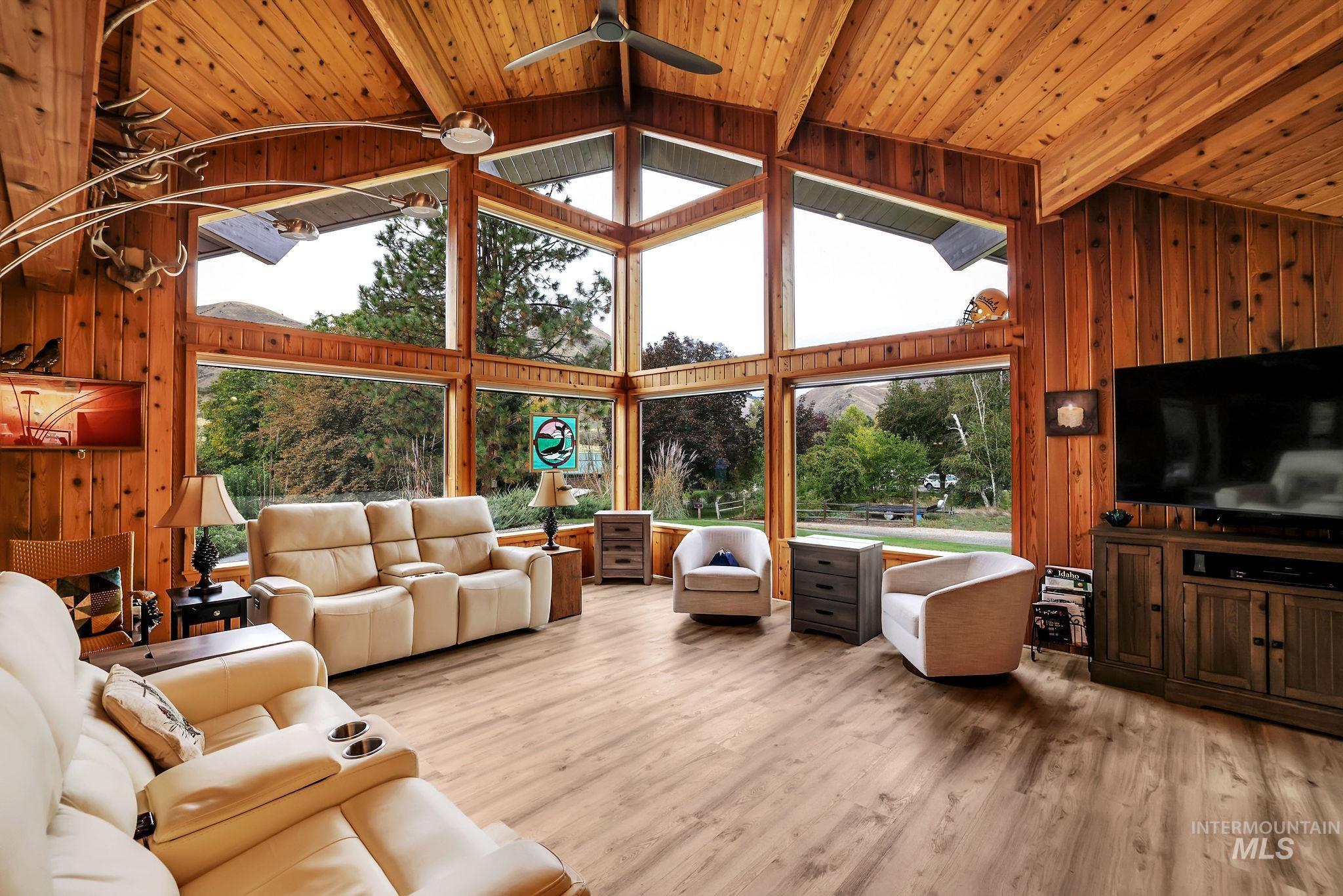 Living area featuring wooden walls, ceiling fan, light wood-style flooring, high vaulted ceiling, and a wood ceiling with exposed beams