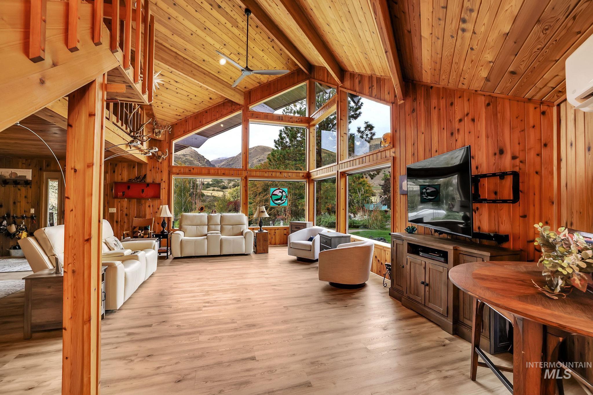 Living area with wooden walls, high vaulted ceiling, light wood-style flooring, a wooden ceiling with exposed beams, and ceiling fan