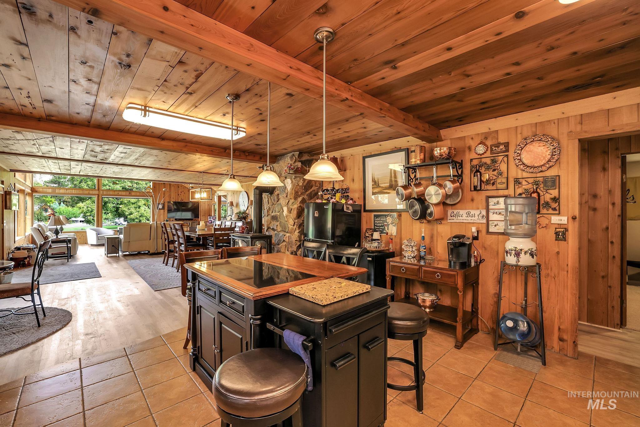 Kitchen featuring decorative light fixtures, wooden walls, a breakfast bar area, a wood ceiling with exposed beams, and light tile patterned floors