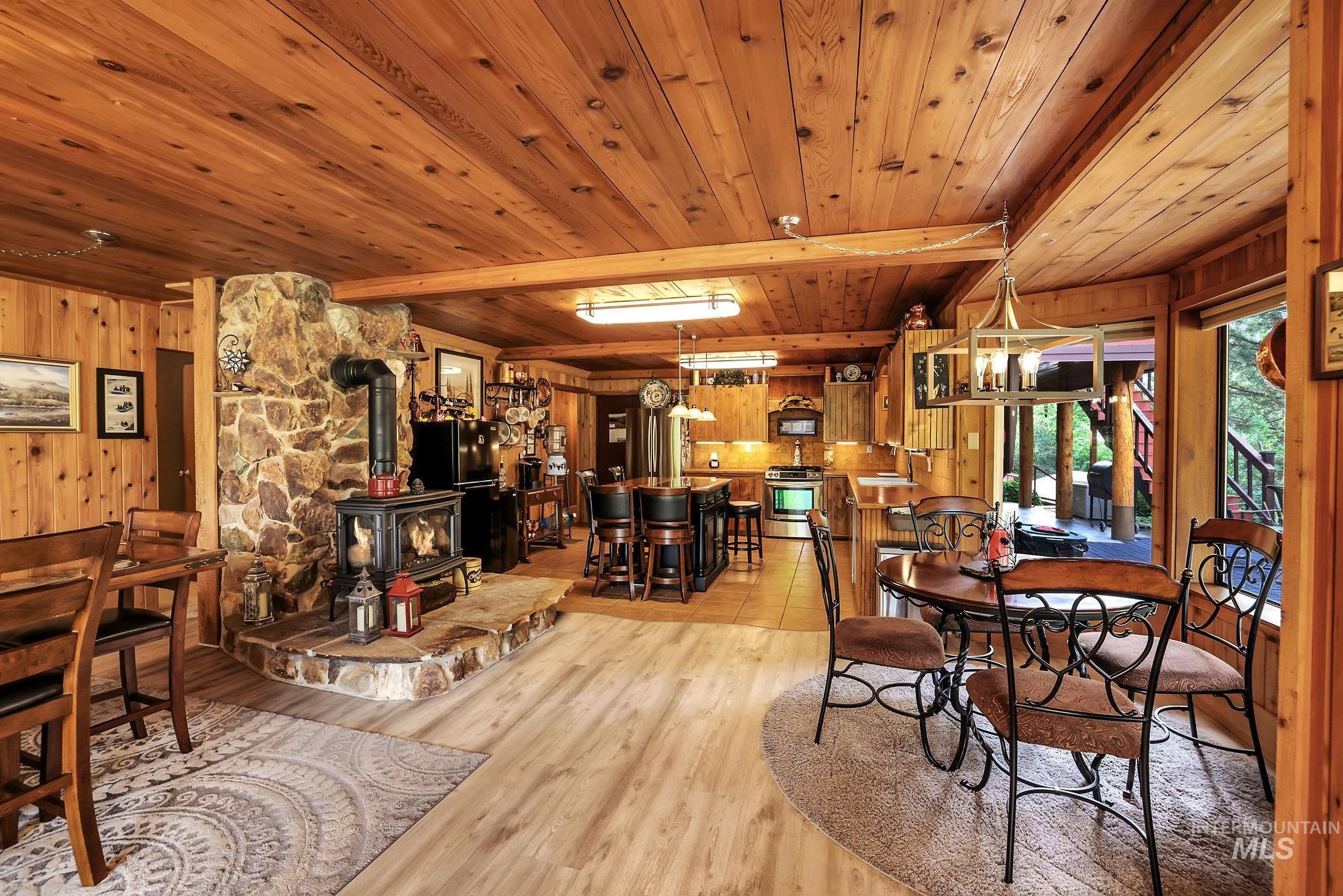 Dining space with wood walls, a wood stove, light wood-style flooring, a wooden ceiling with exposed beams, and a chandelier