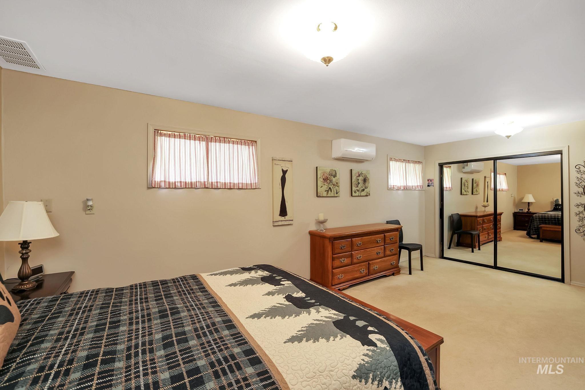 Carpeted bedroom with a closet, multiple windows, and a wall mounted air conditioner