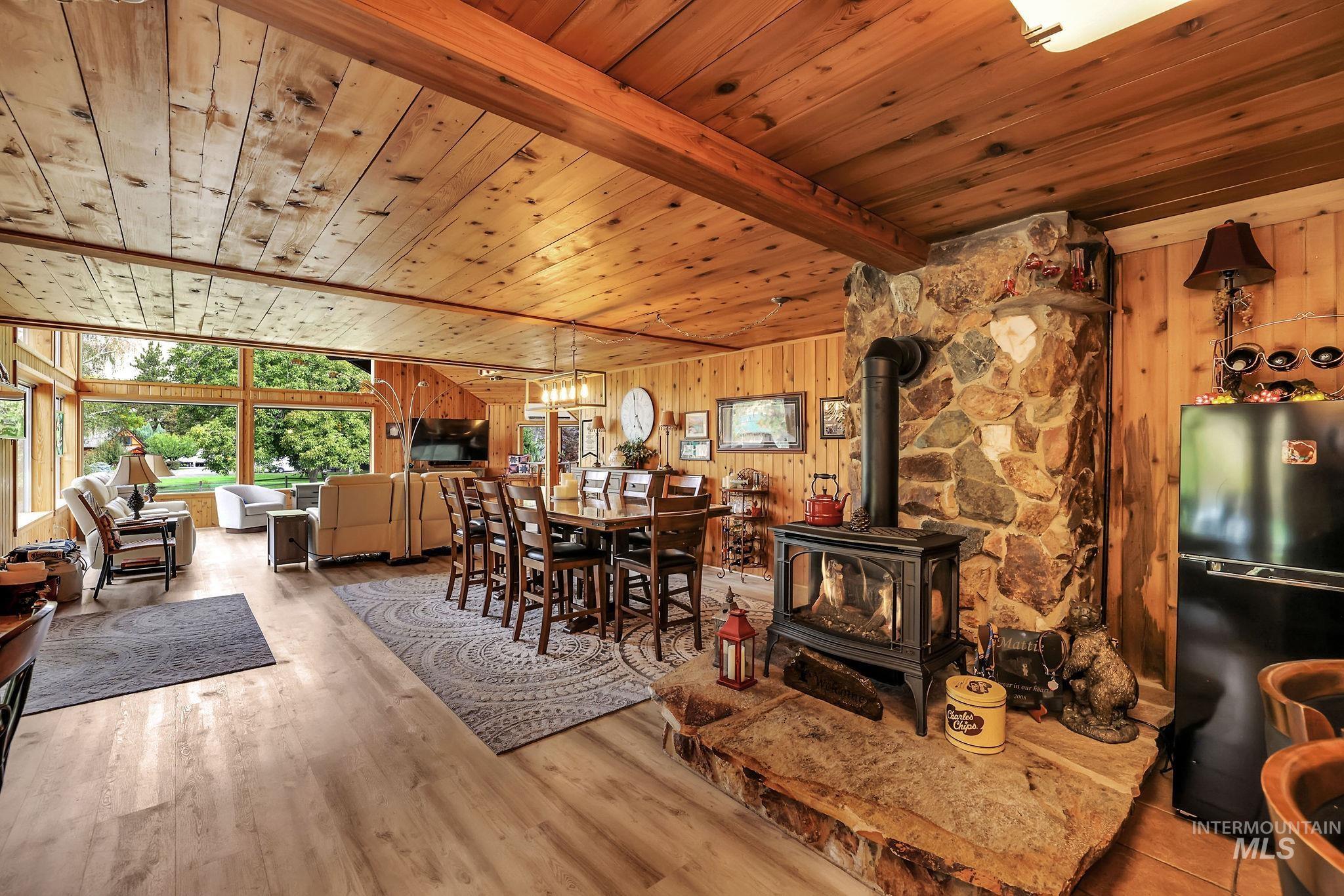 Dining room featuring wooden walls, a wood stove, a wood ceiling with exposed beams, and wood finished floors
