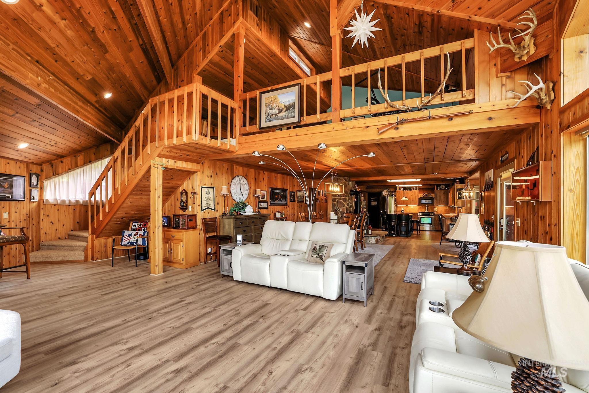 Living room with a wooden ceiling with exposed beams, stairs, wood walls, wood finished floors, and a high ceiling