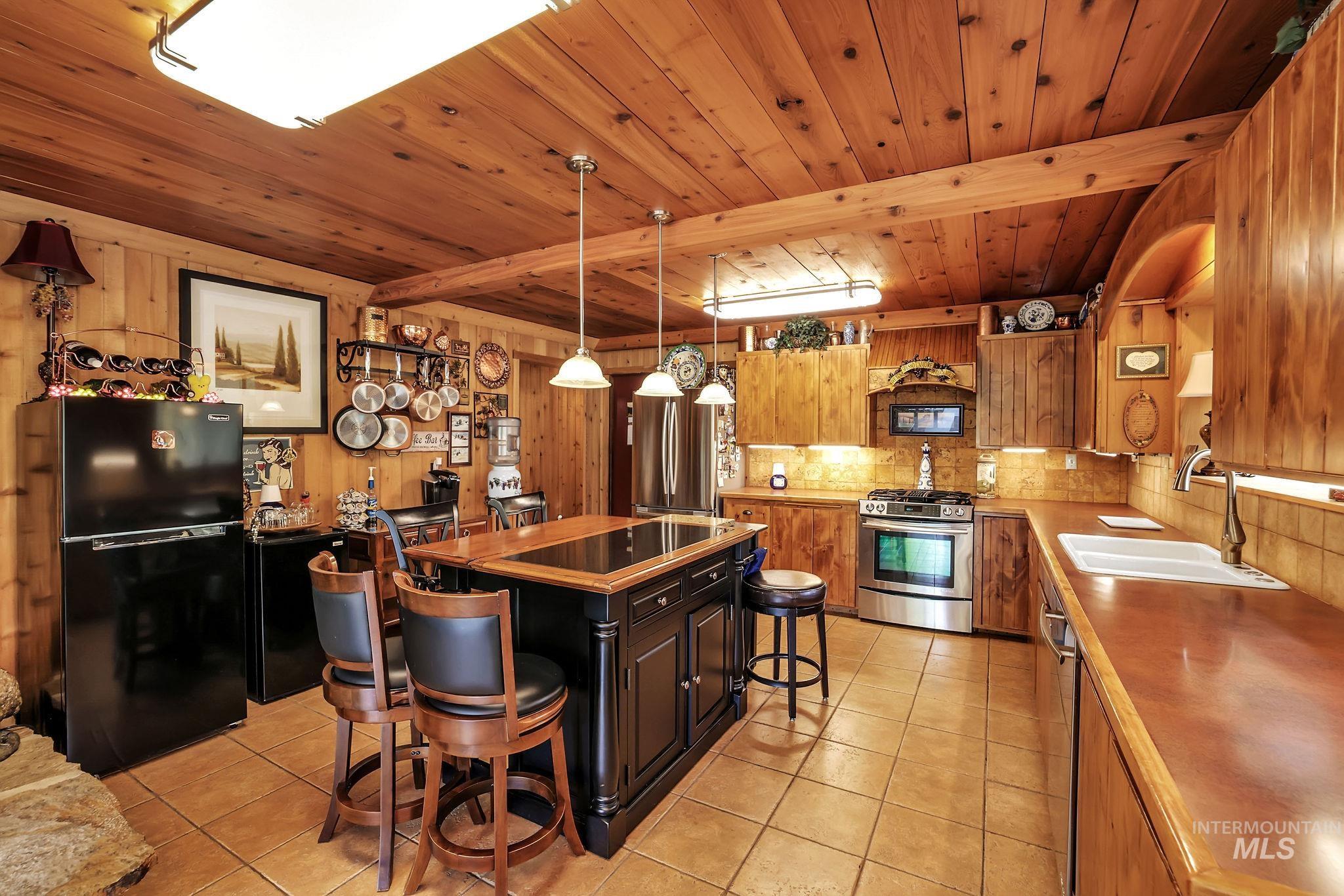 Kitchen with a breakfast bar, appliances with stainless steel finishes, light tile patterned floors, open shelves, and pendant lighting