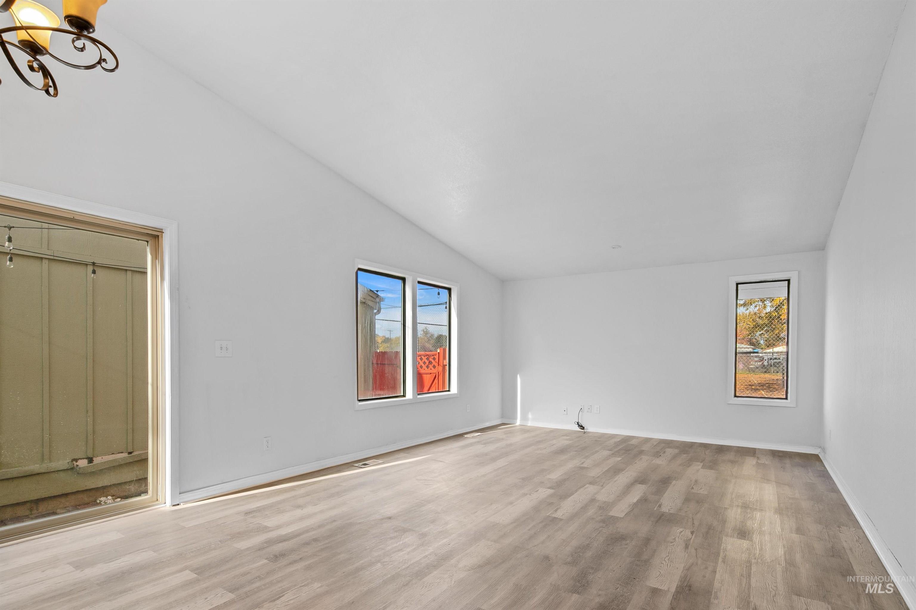Unfurnished living room with lofted ceiling, light wood-type flooring, and plenty of natural light