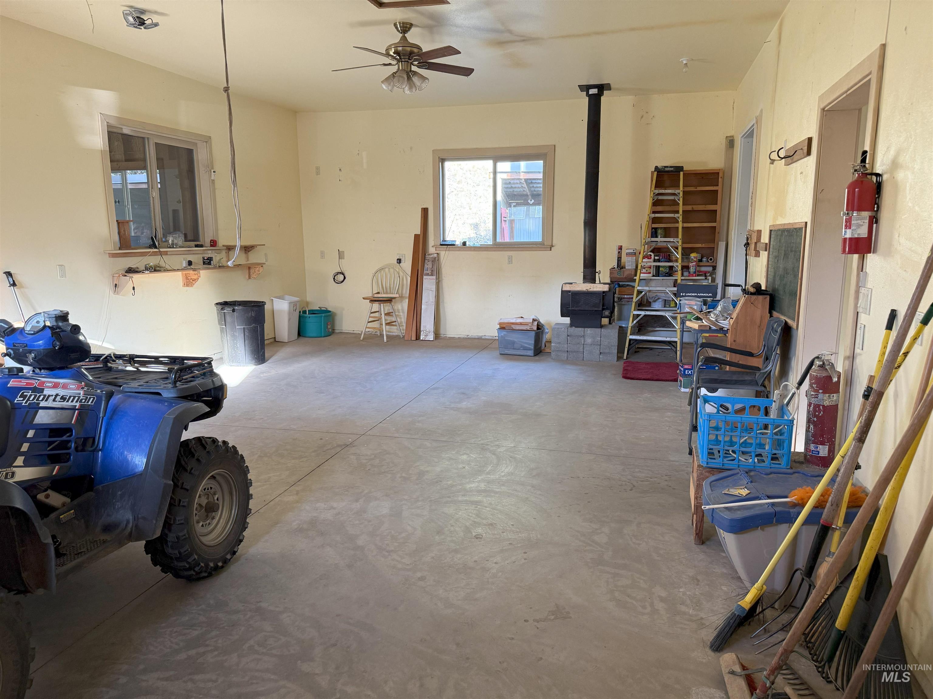 Miscellaneous room with unfinished concrete floors, a wood stove, and a ceiling fan