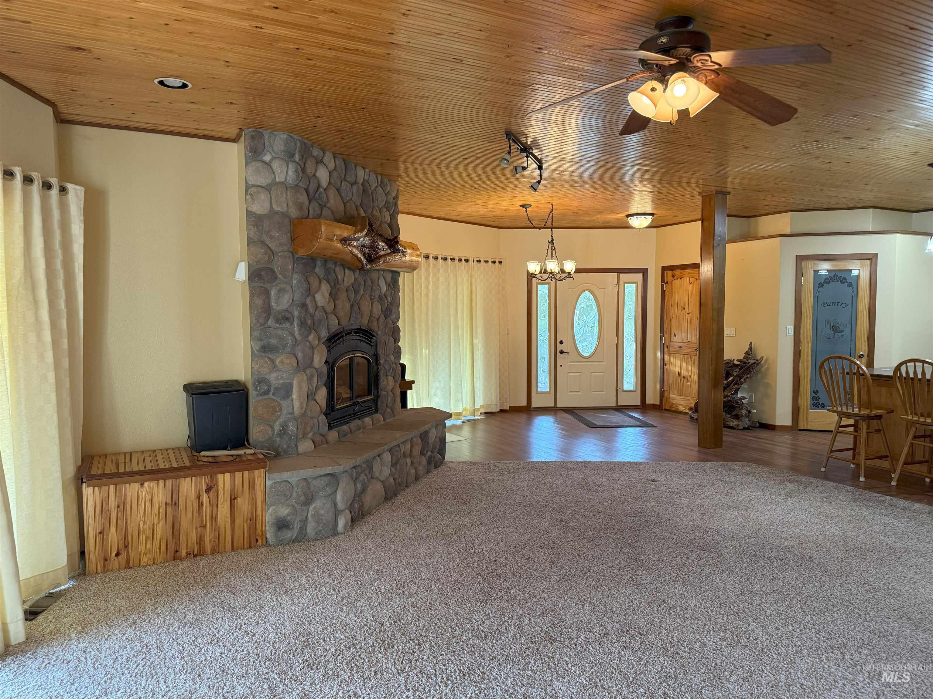 Unfurnished living room with carpet floors, wood ceiling, a stone fireplace, and a ceiling fan