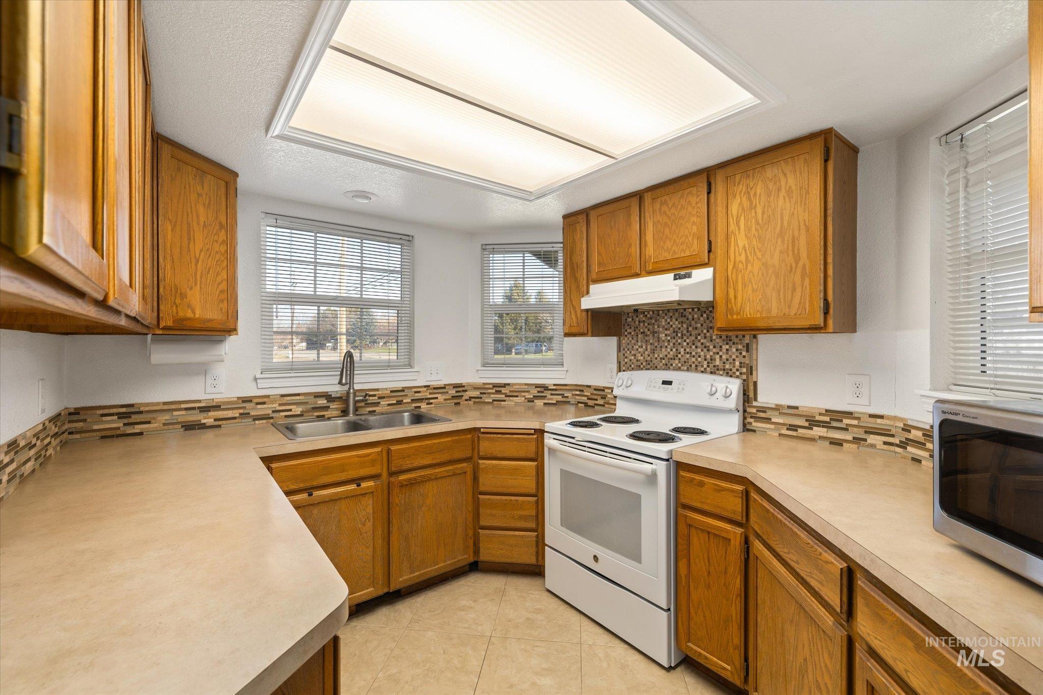Kitchen featuring electric stove, brown cabinetry, light countertops, and stainless steel microwave