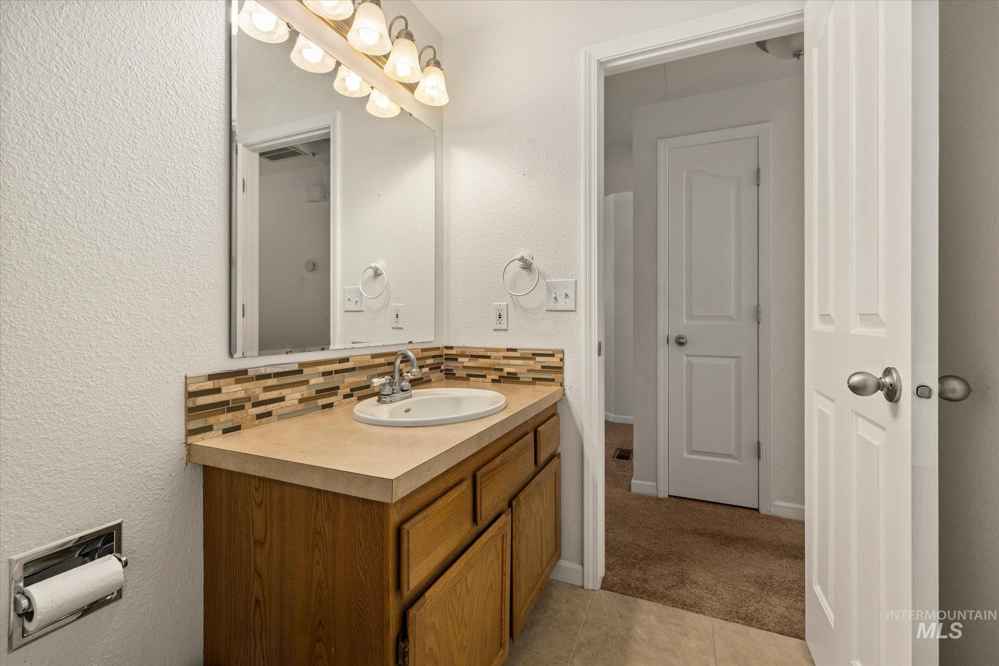 Bathroom with decorative backsplash, a textured wall, vanity, light carpet, and light tile patterned floors