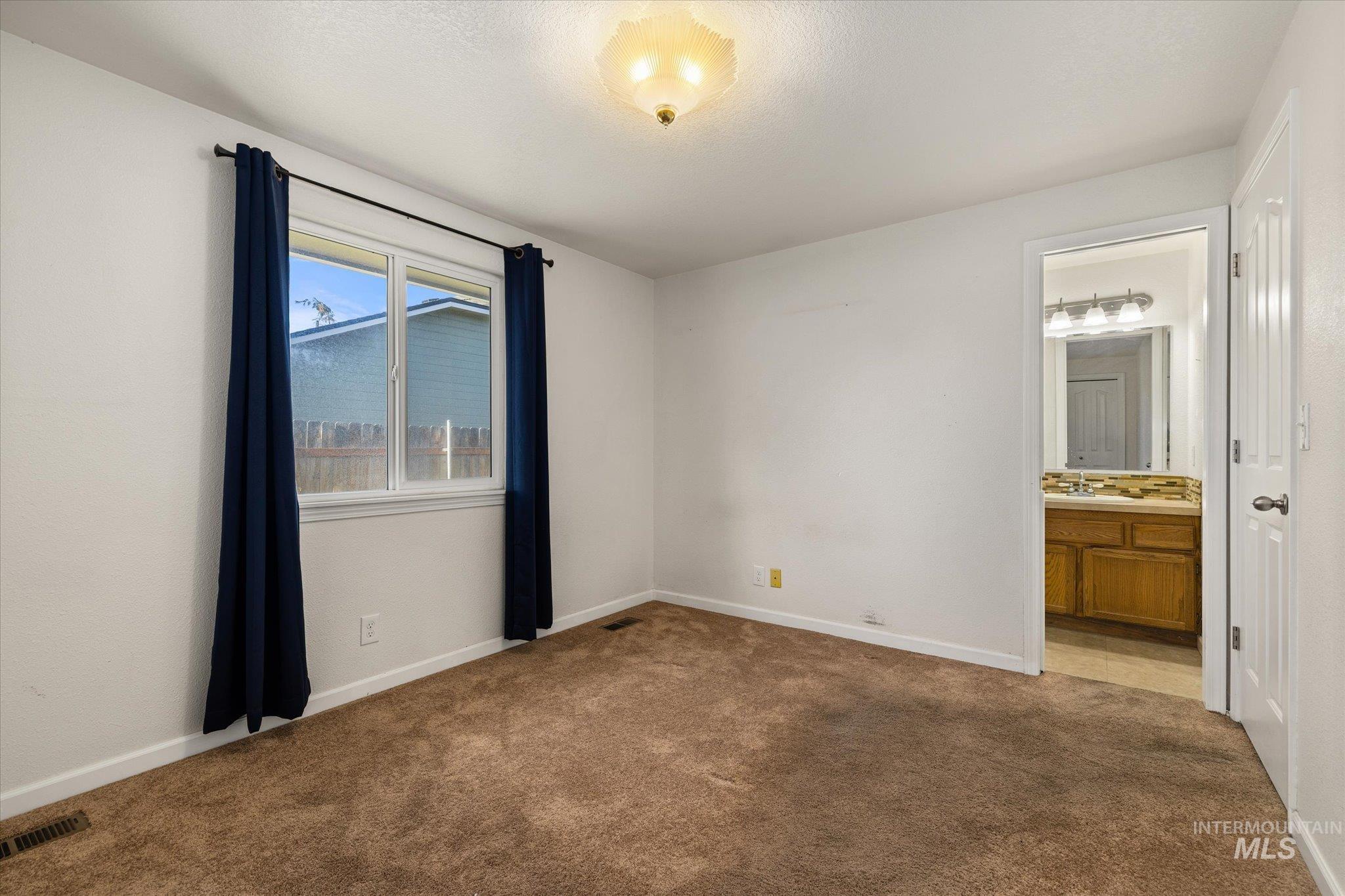 Unfurnished bedroom featuring dark colored carpet and connected bathroom