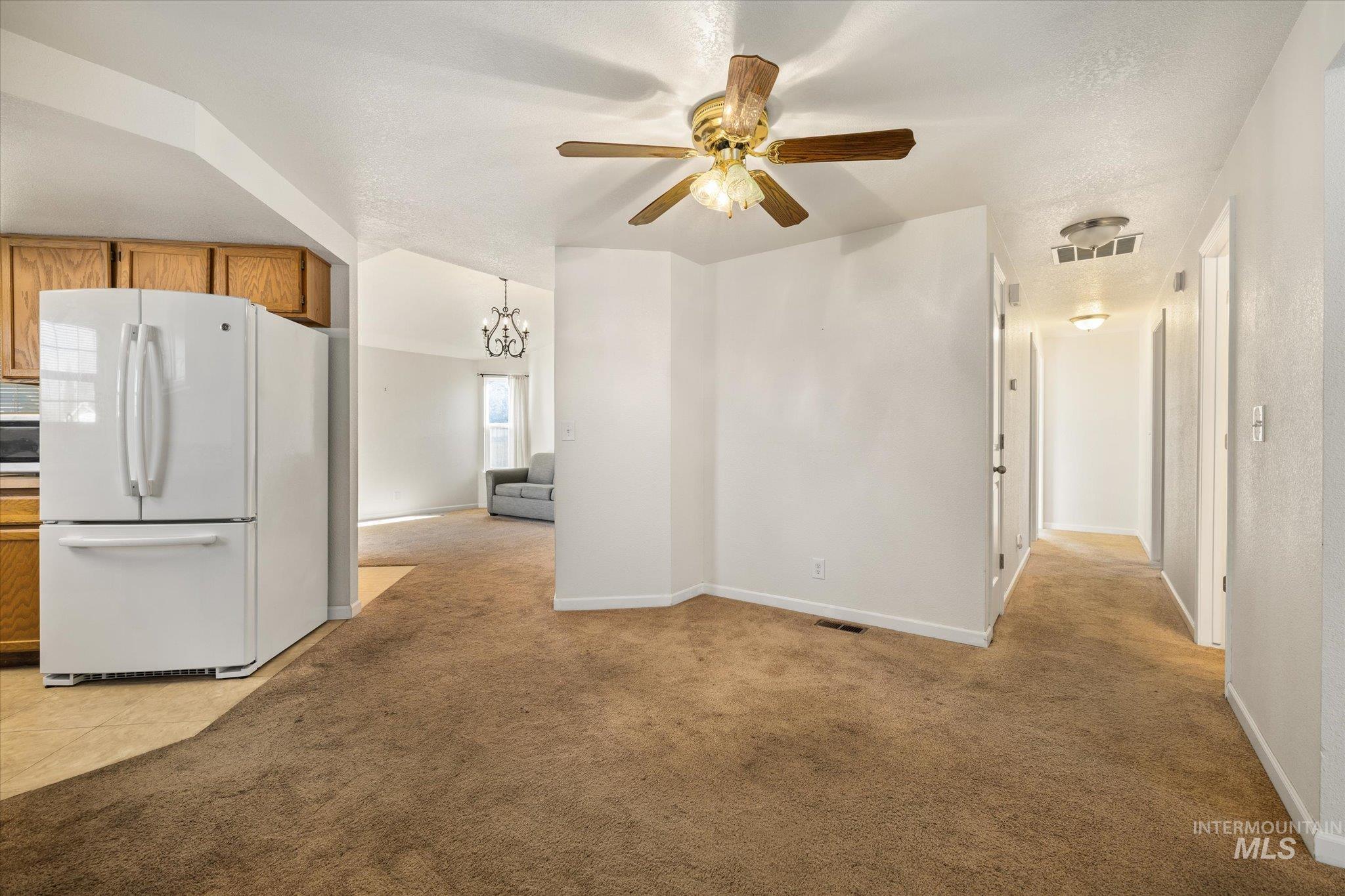 Kitchen featuring brown cabinets, freestanding refrigerator, a chandelier, light colored carpet, and ceiling fan