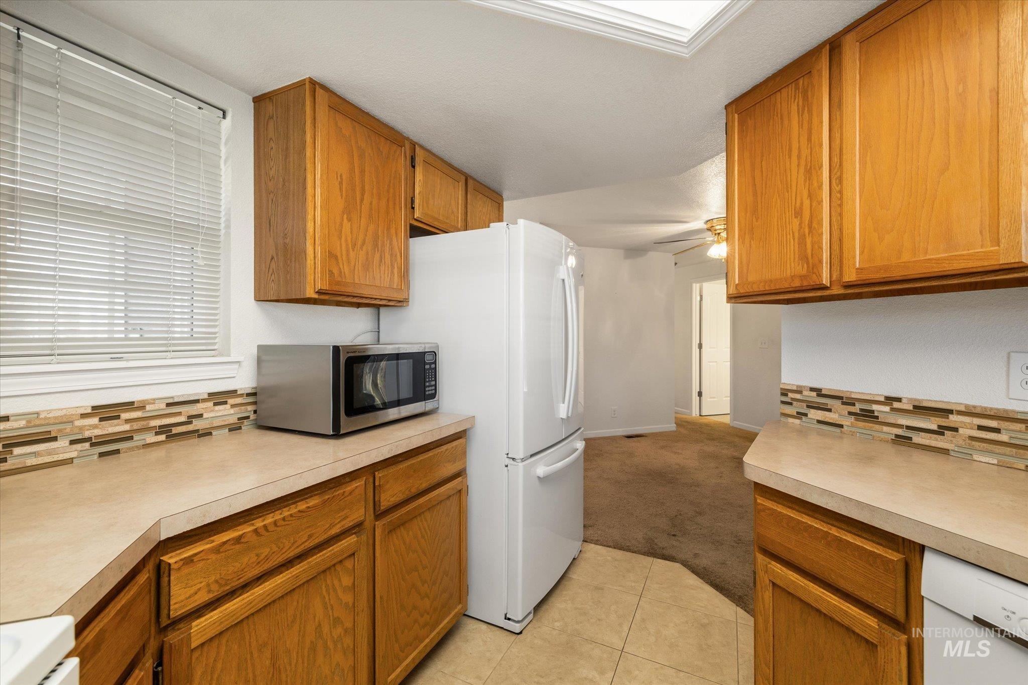 Kitchen featuring backsplash, light carpet, white appliances, and brown cabinets