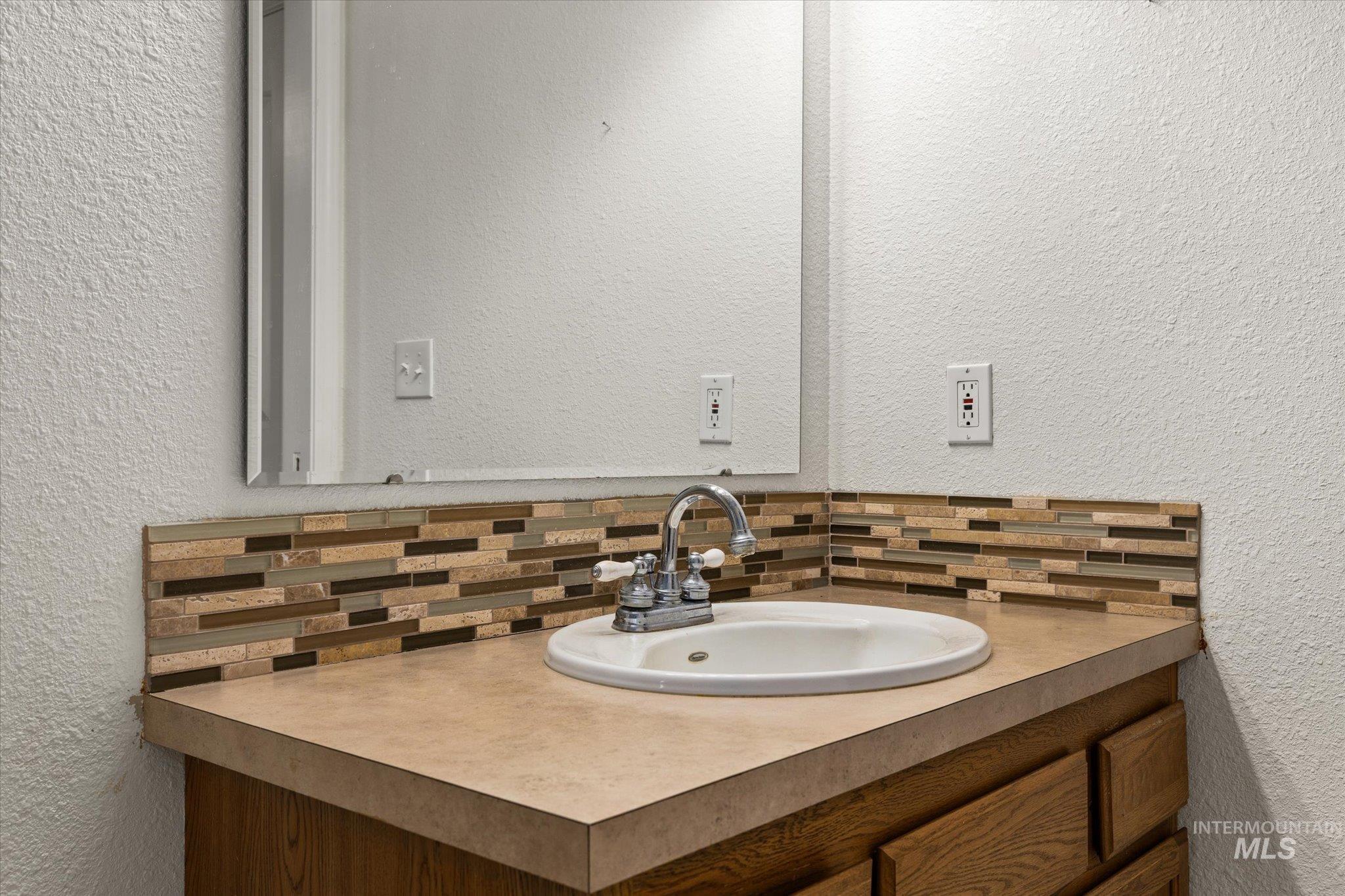 Bathroom with a textured wall, vanity, and decorative backsplash