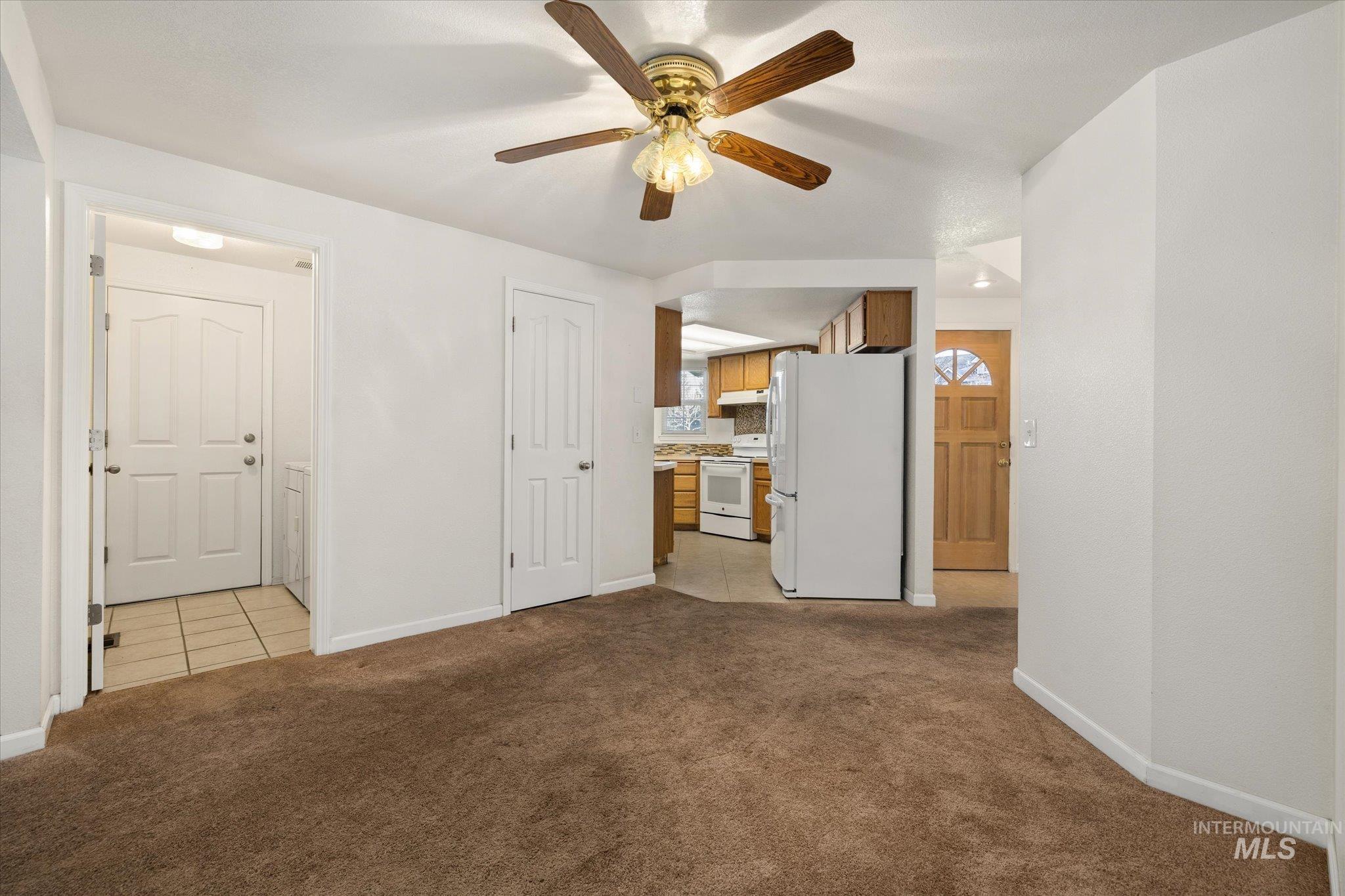 Unfurnished living room with light carpet, ceiling fan, and light tile patterned floors