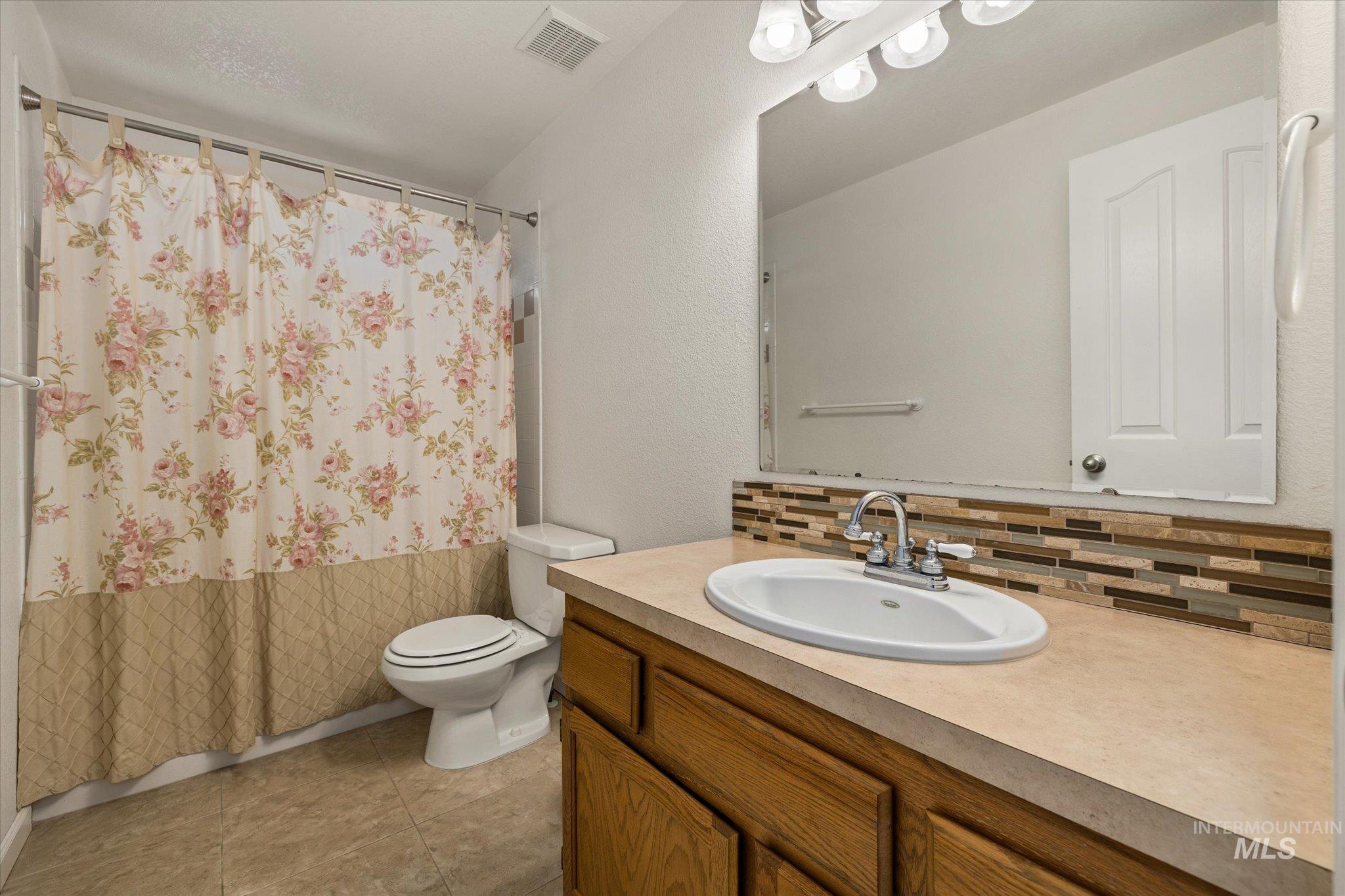 Full bath with a shower with curtain, vanity, a textured wall, and tasteful backsplash