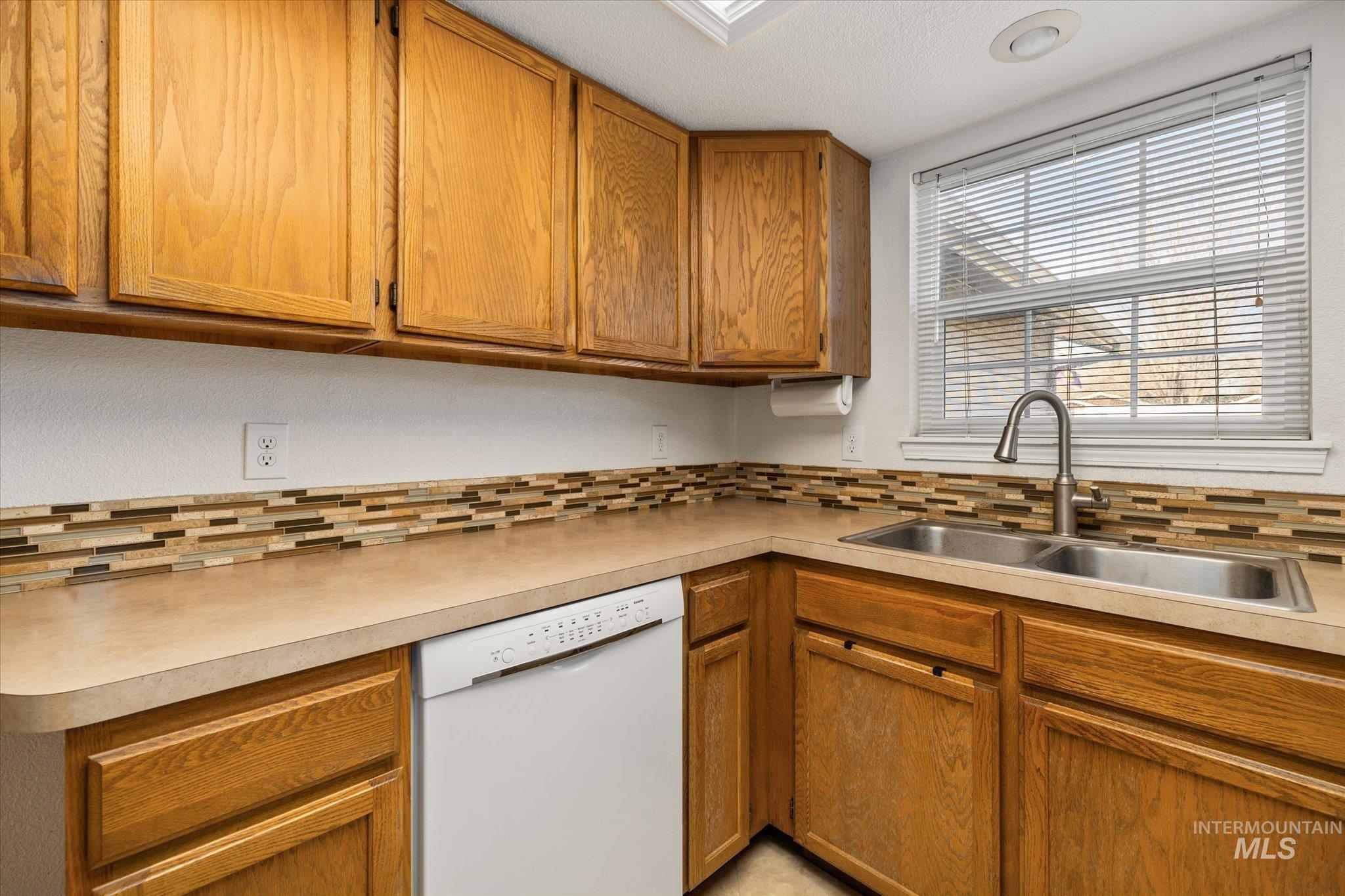 Kitchen featuring brown cabinets, white dishwasher, light countertops, and a textured ceiling