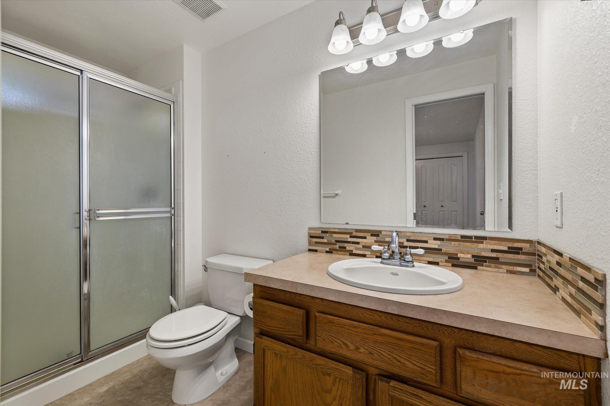 Bathroom featuring a textured wall, vanity, a stall shower, and tasteful backsplash