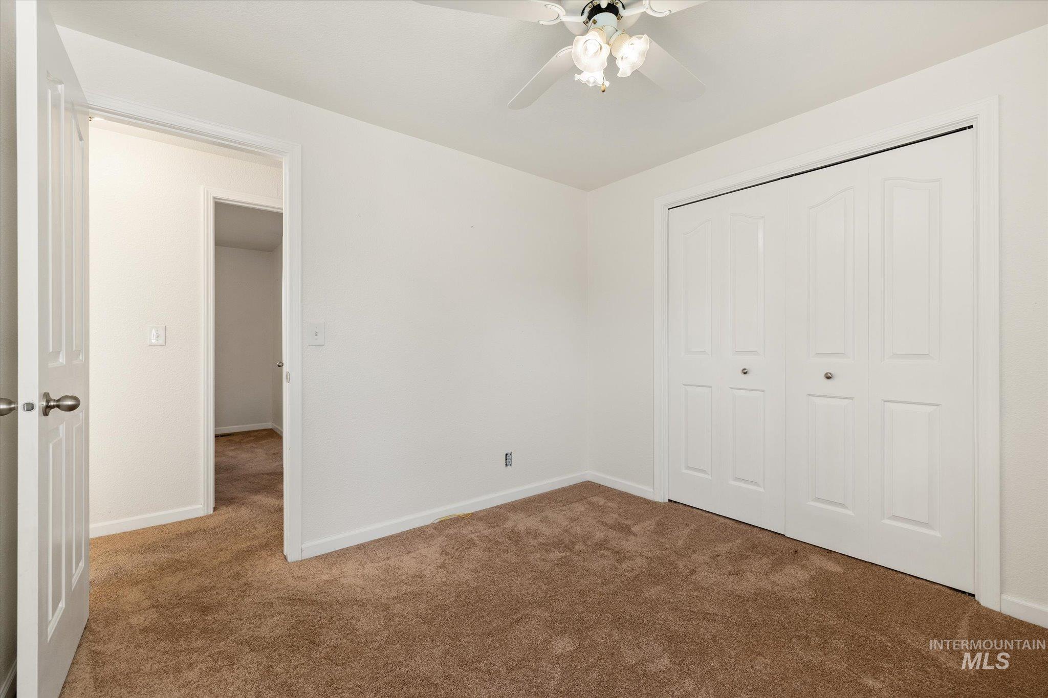 Unfurnished bedroom featuring dark colored carpet, a closet, and a ceiling fan