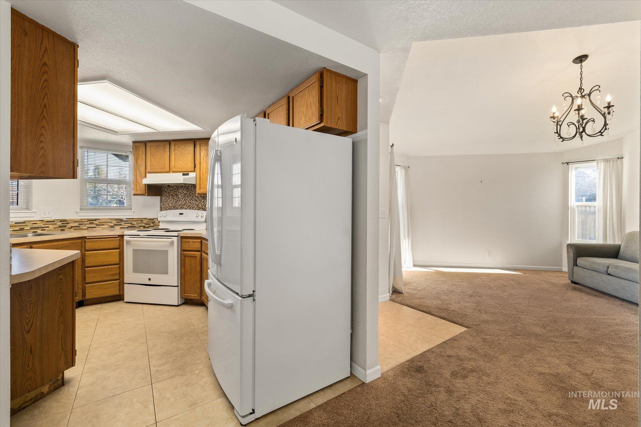 Kitchen featuring white appliances, light colored carpet, light countertops, open floor plan, and light tile patterned floors