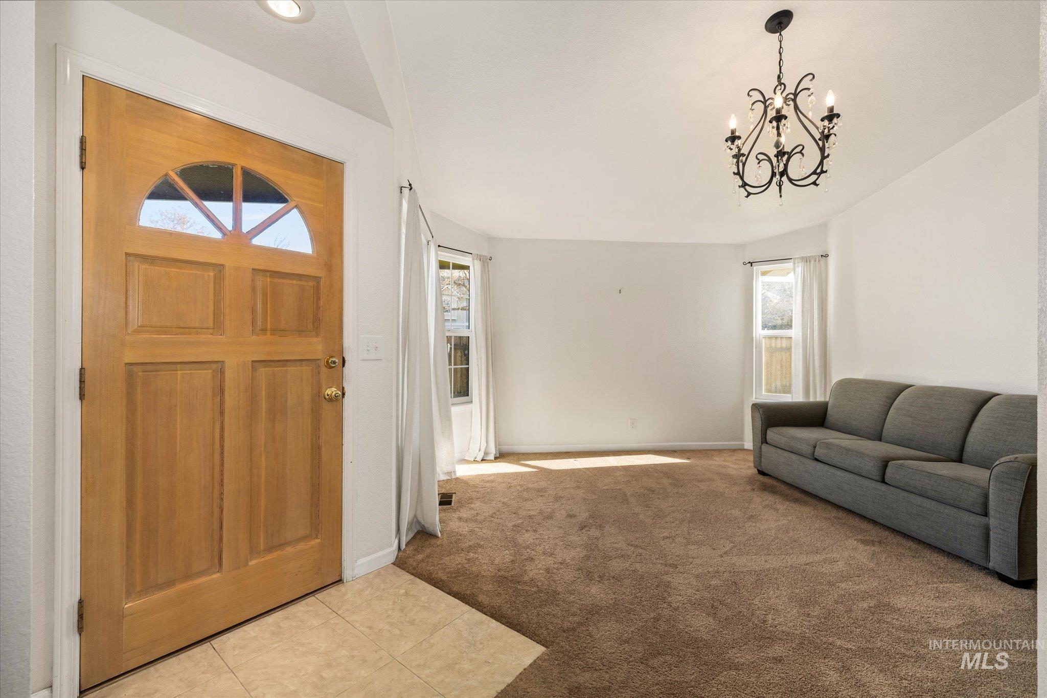 Carpeted foyer featuring healthy amount of natural light, a chandelier, and tile patterned flooring
