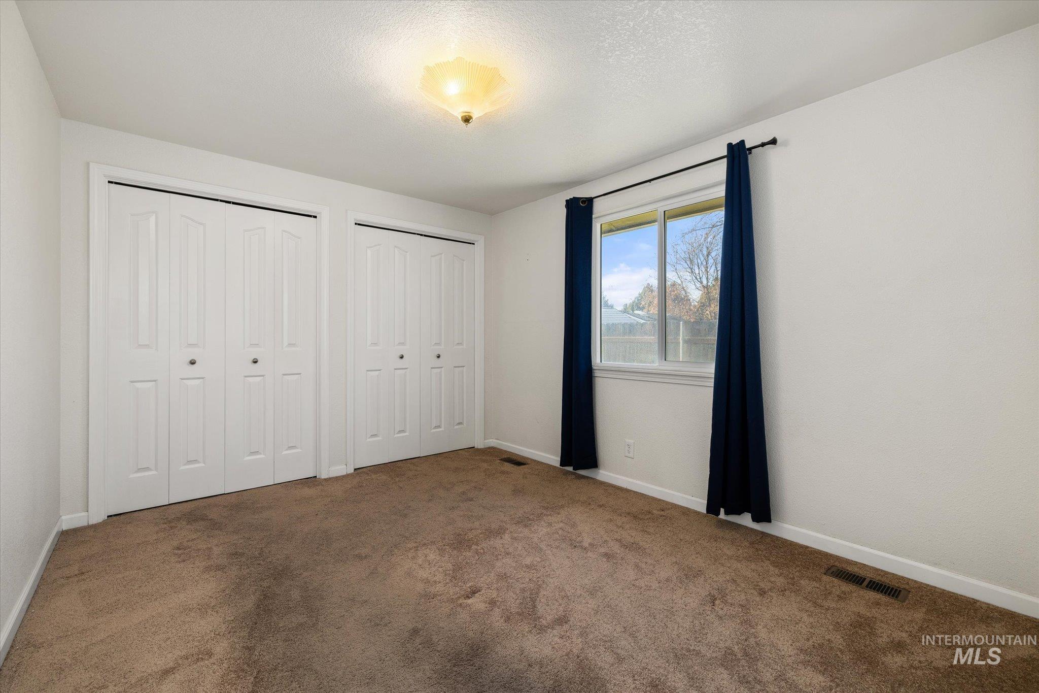 Unfurnished bedroom with two closets, carpet flooring, and a textured ceiling