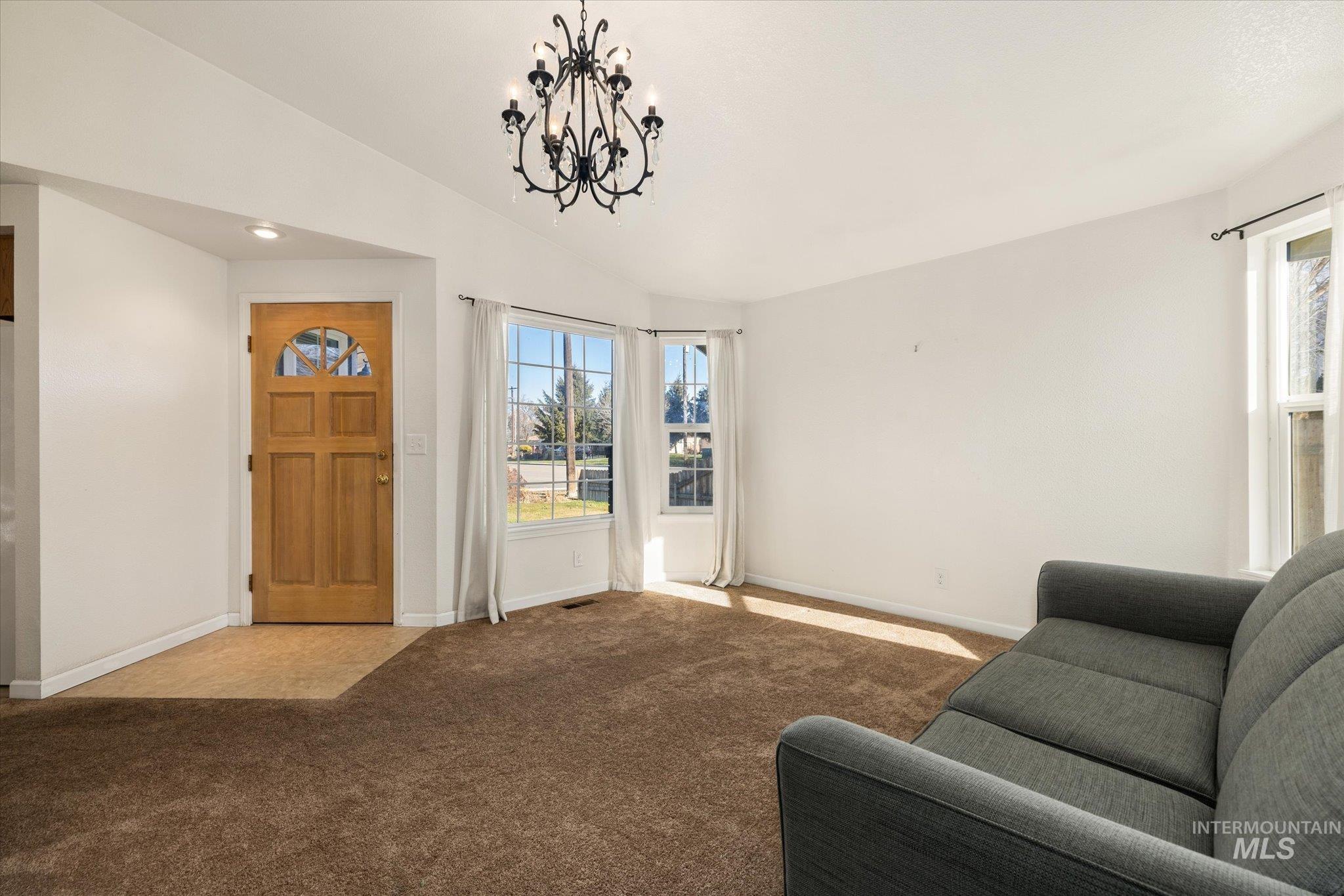 Living area featuring vaulted ceiling, light carpet, and a chandelier