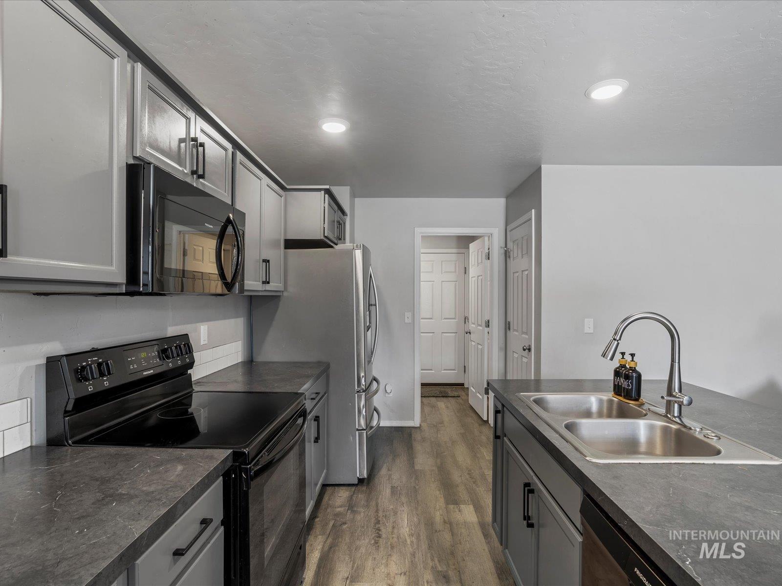 Kitchen with black appliances, dark wood-type flooring, dark countertops, and recessed lighting